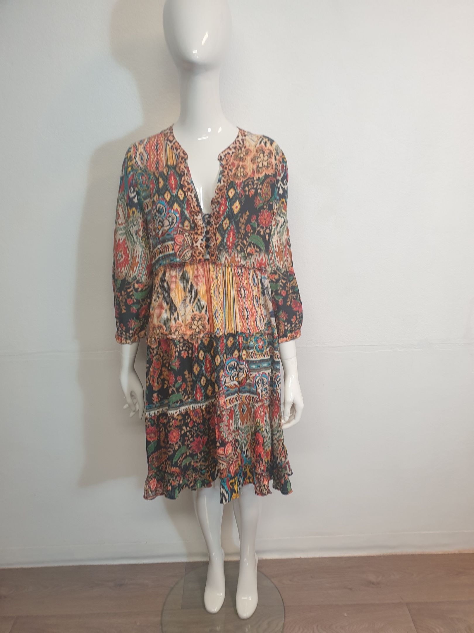 A colorful floral print dress on a mannequin, with long sleeves, a V-neck, and a tiered skirt.