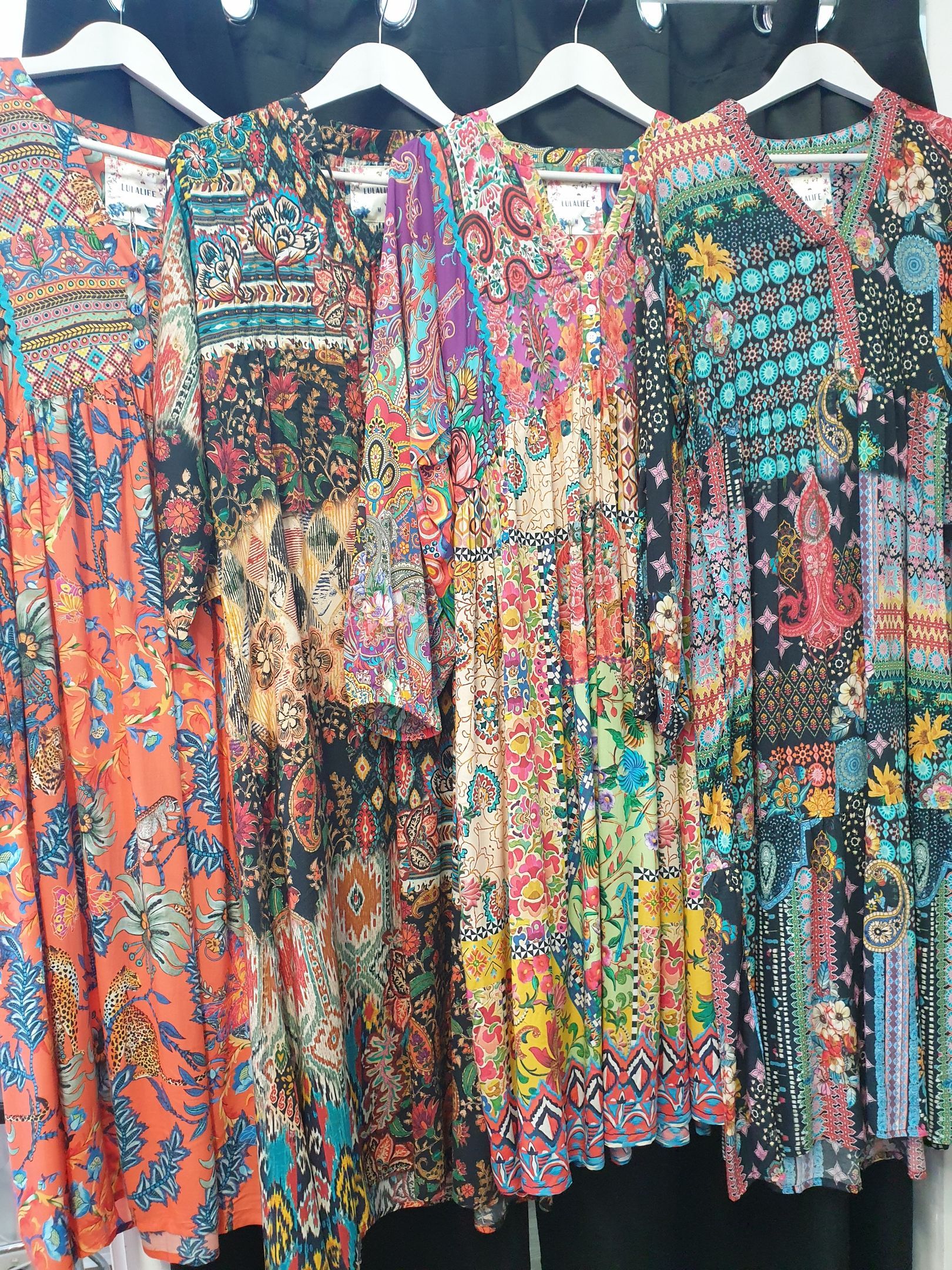 Dresses on hangers with colorful patchwork floral patterns.