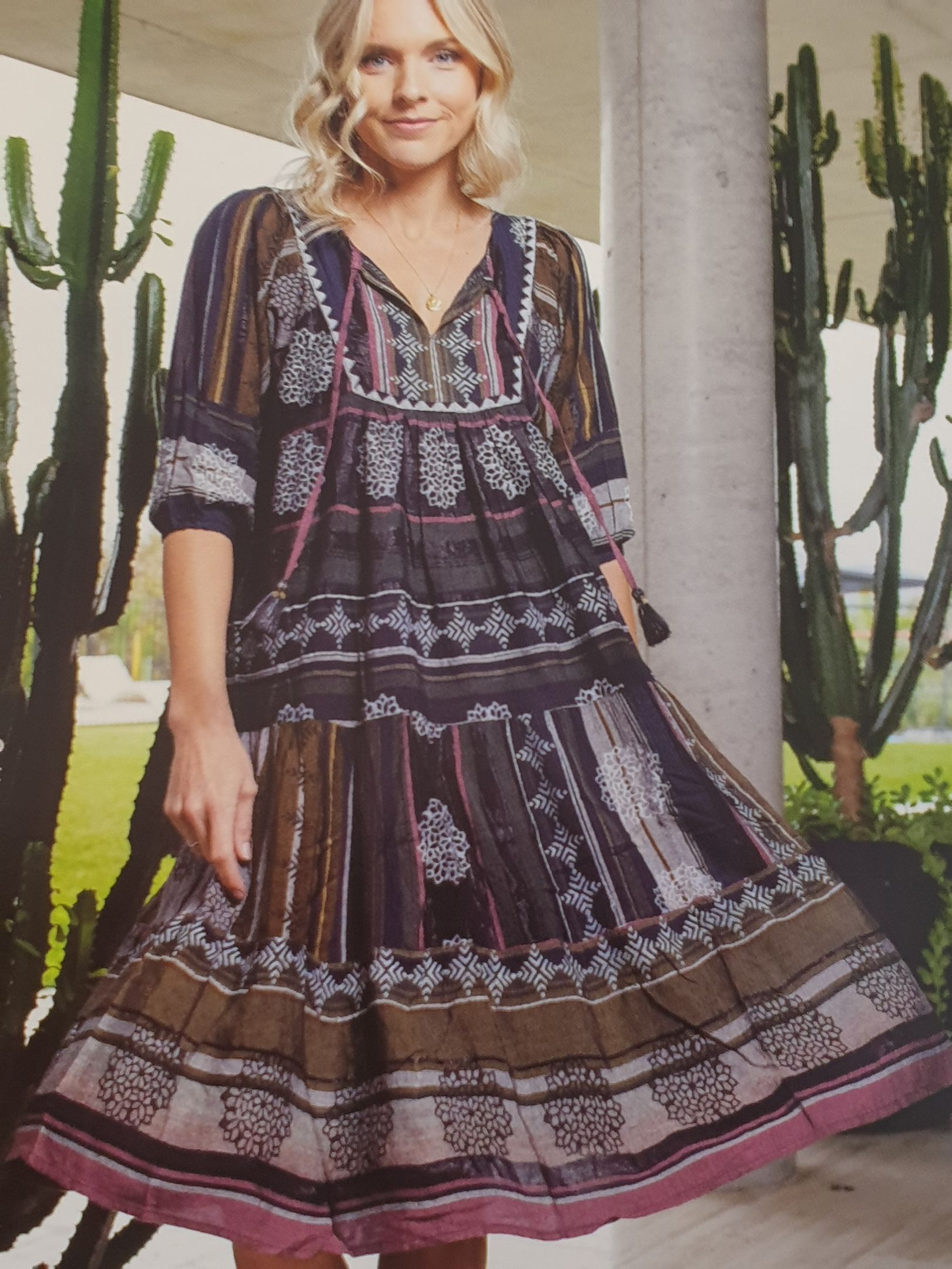 Woman in patterned dress, standing outdoors near cacti and a pillar.
