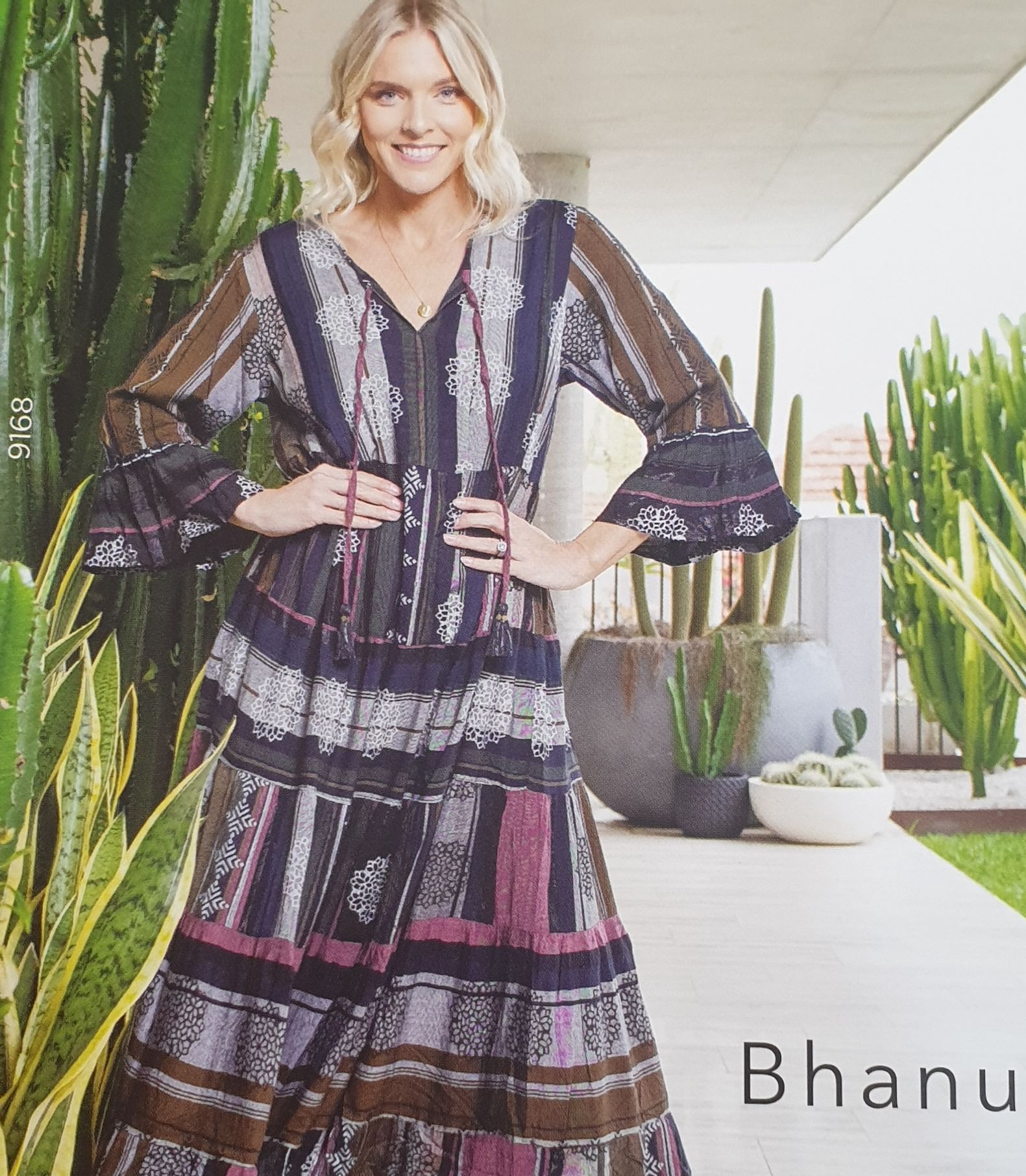 Woman wearing patterned maxi dress, smiling, standing outside near cacti.