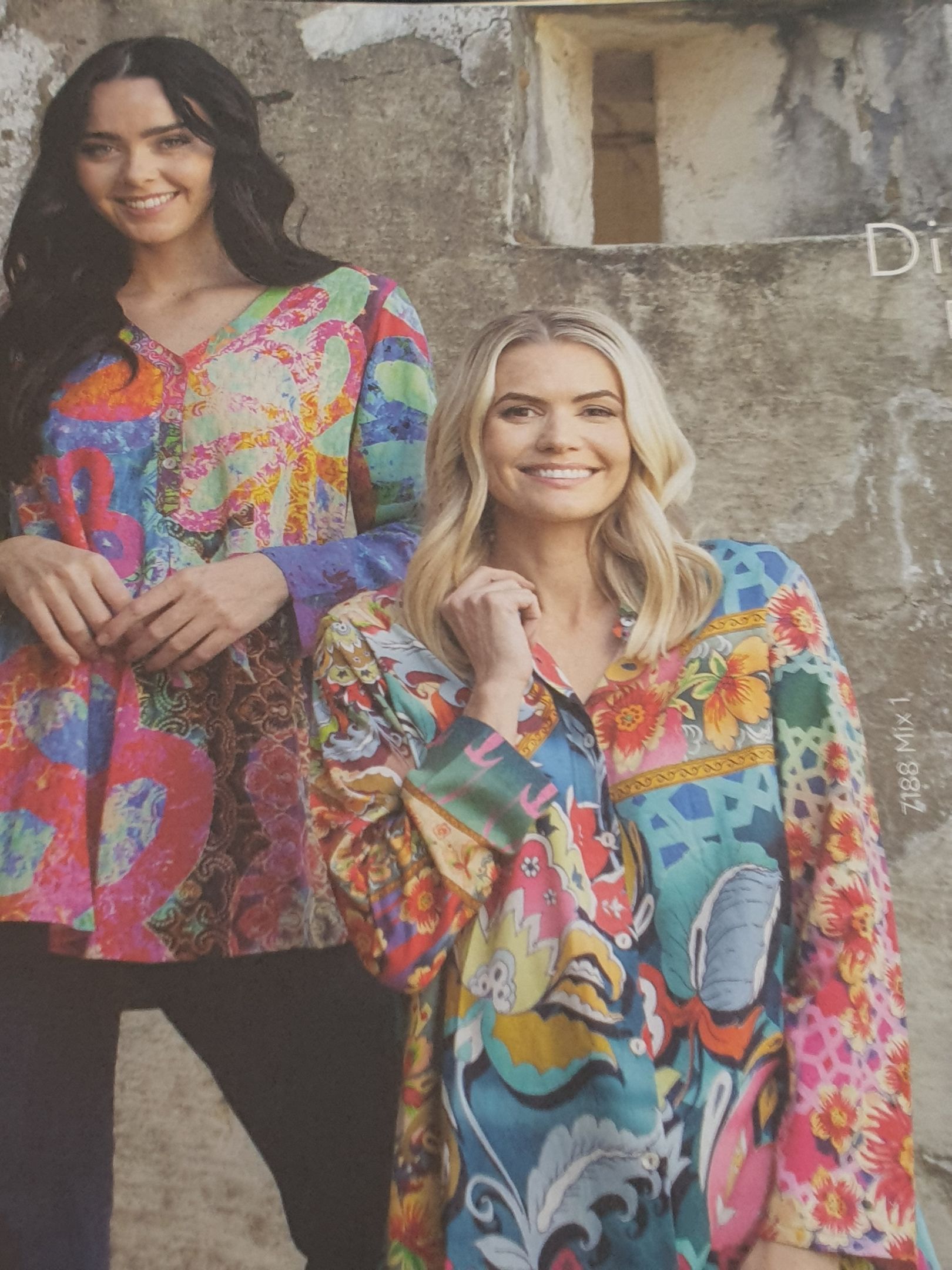Two women in colorful patterned shirts smiling against a weathered wall.