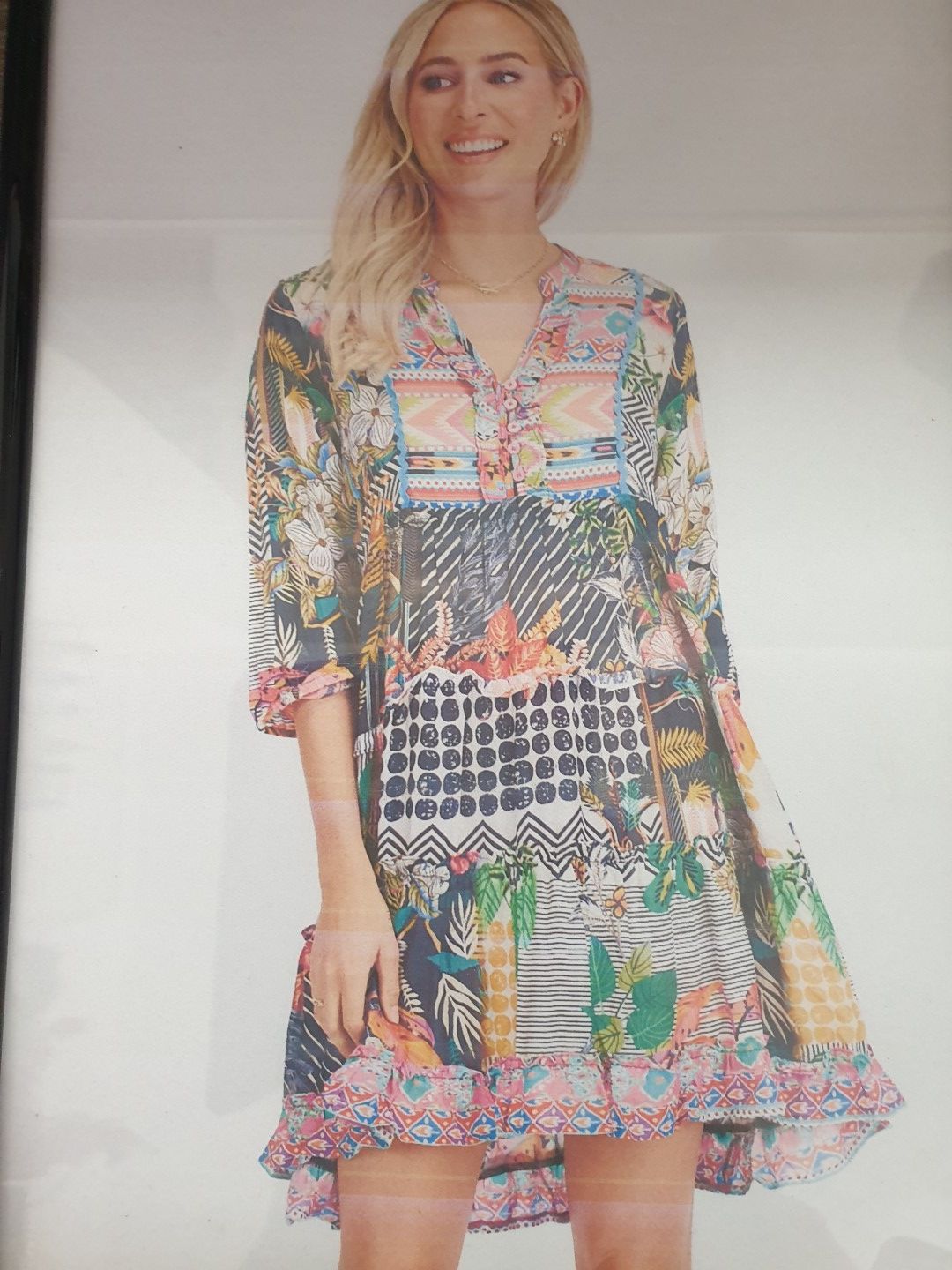 Blonde woman in colorful patterned dress, smiling. Indoors, natural light.