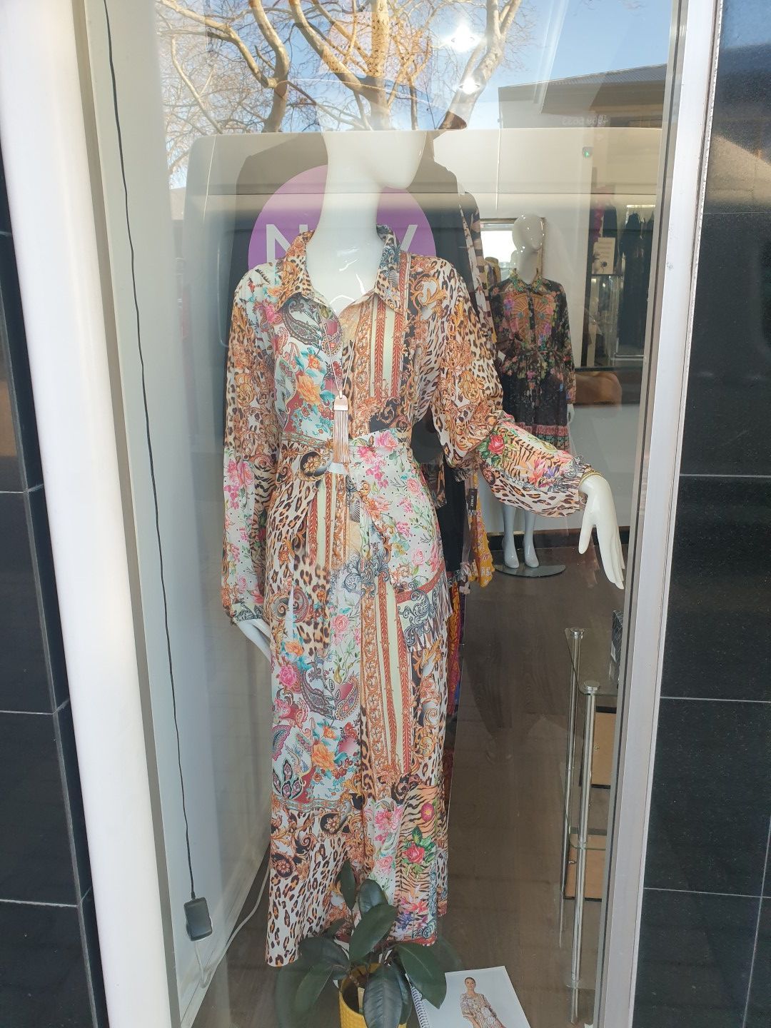 Mannequin in a printed dress in a store window, with a visible belt.