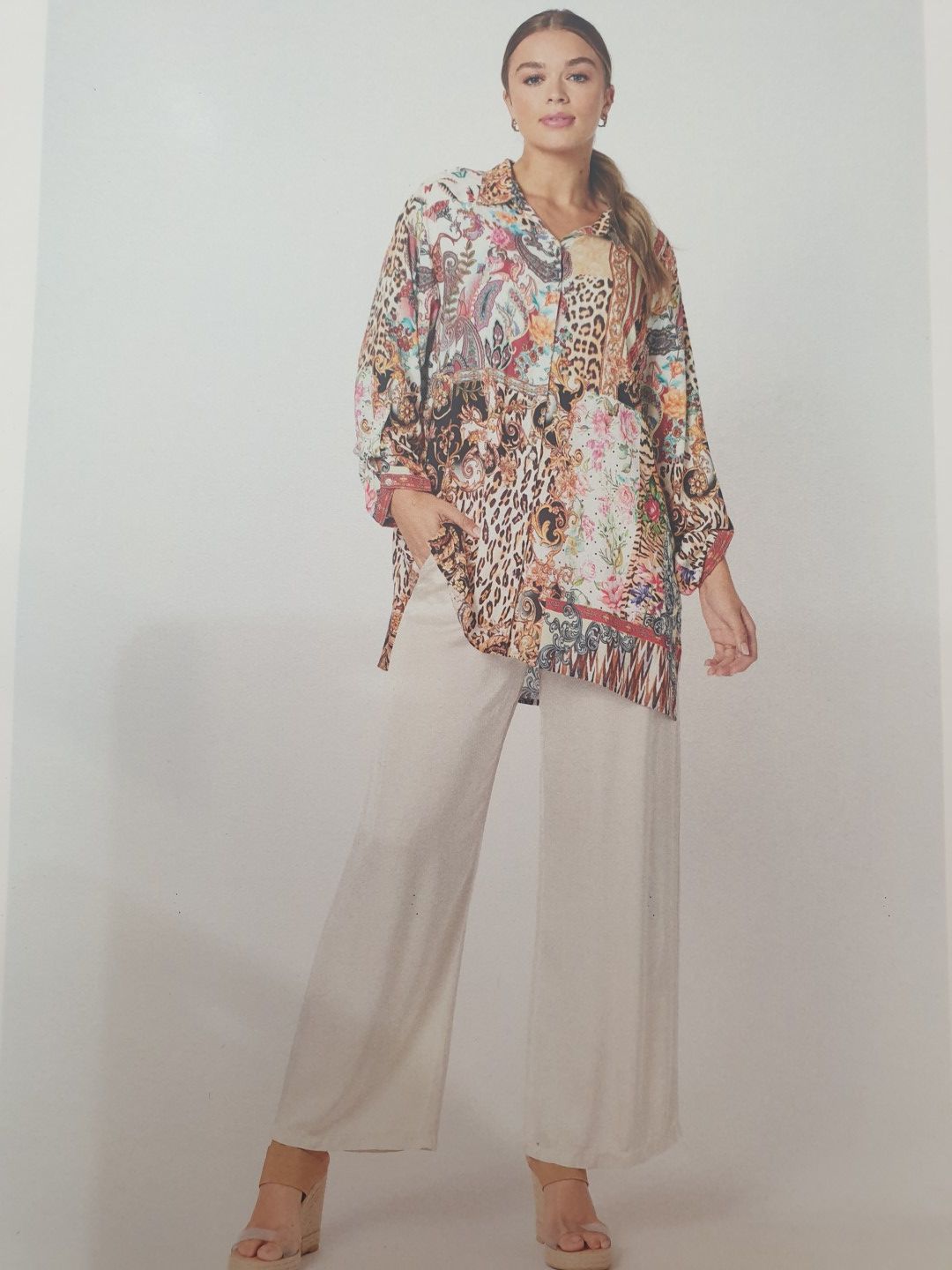 Woman in patterned tunic, white tank top, and wide-leg pants, posing indoors.