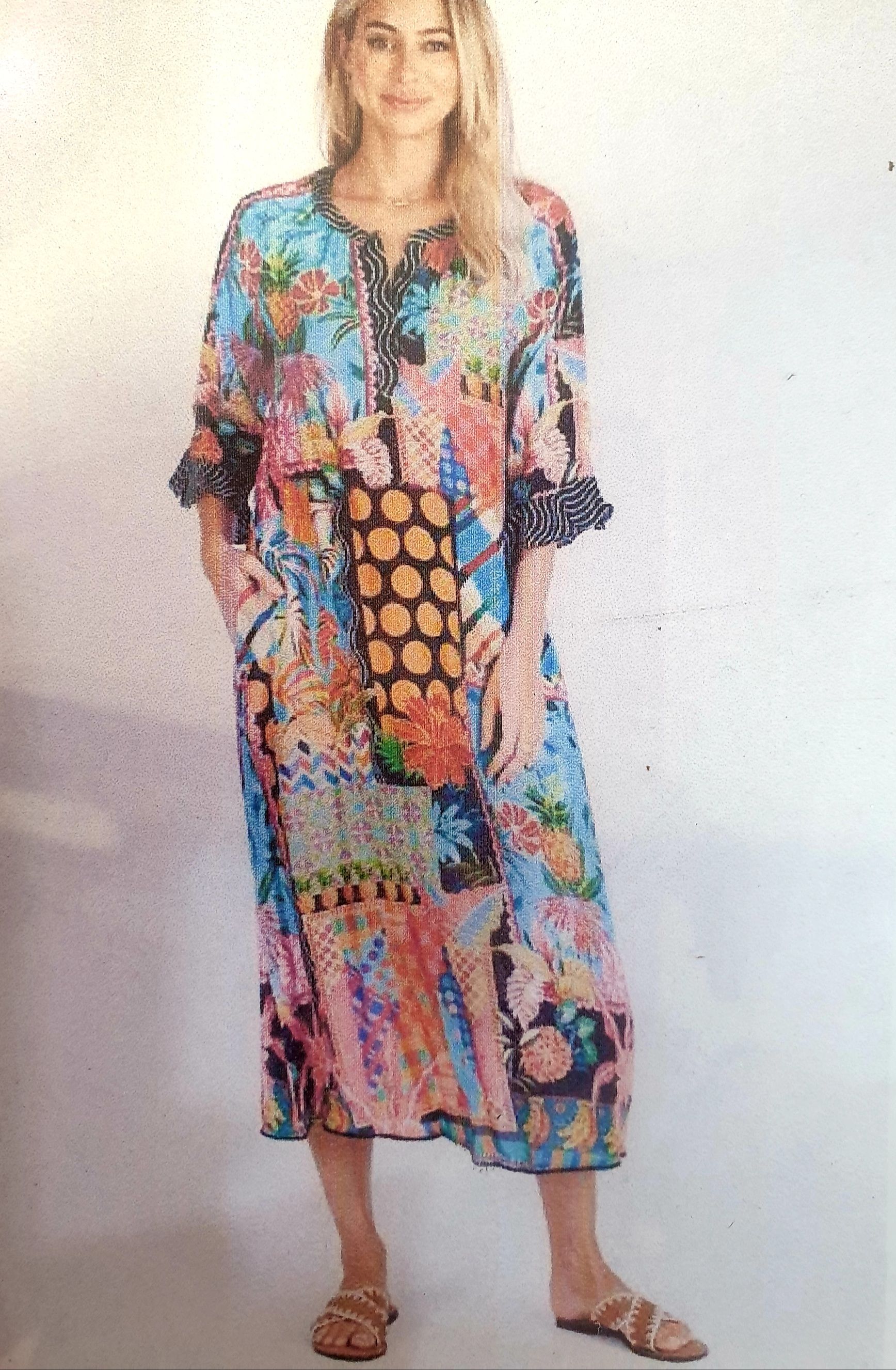 Woman wearing a patchwork maxi dress with floral and polka dot patterns. She stands outside with sandals.