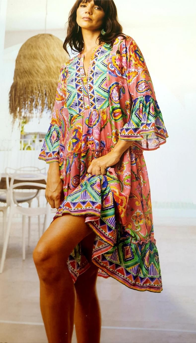 Woman in colorful patterned dress, standing with one leg raised, indoors.