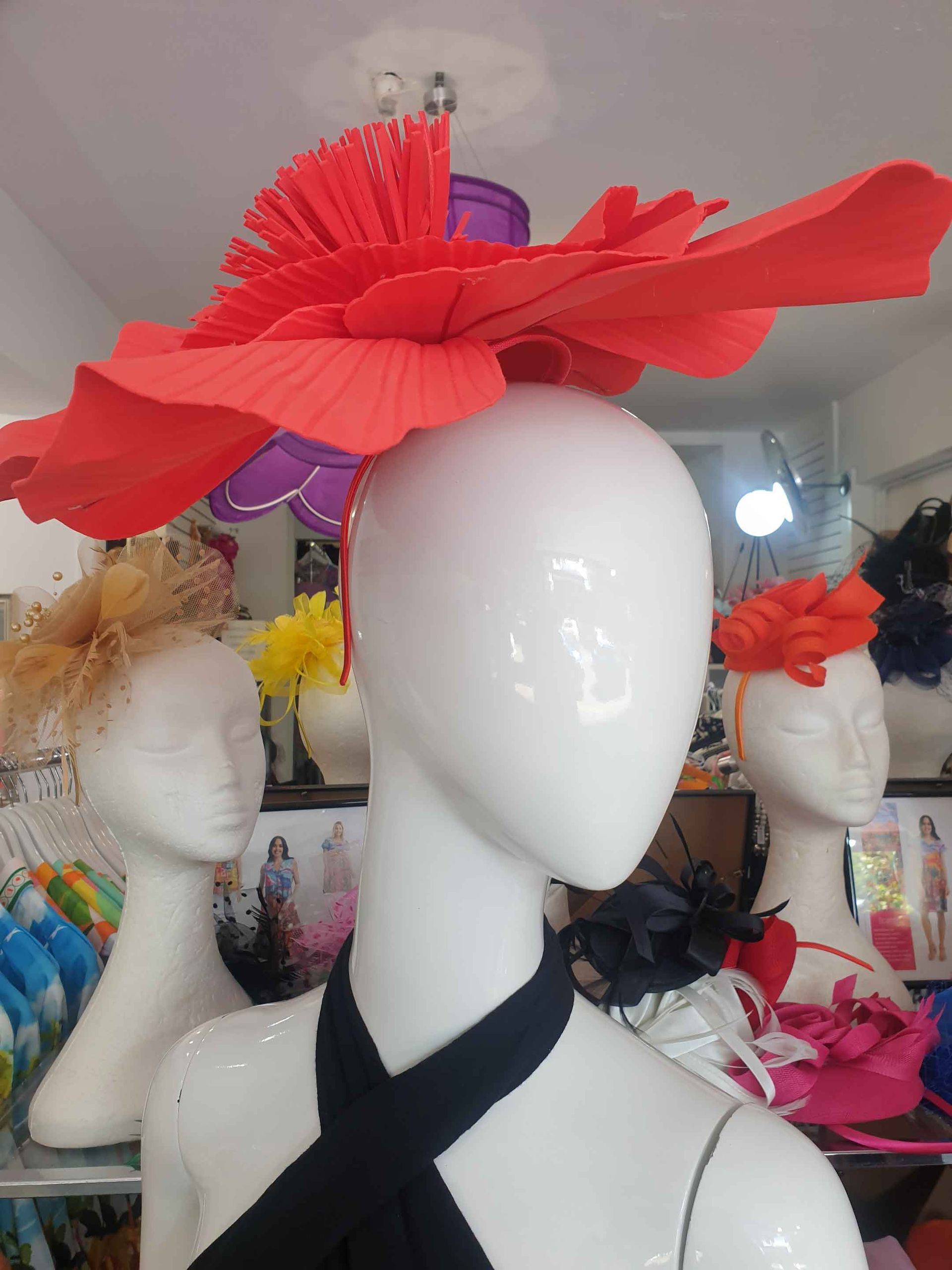 Mannequin wearing a large red flower hat in a shop, other hats visible in the background.