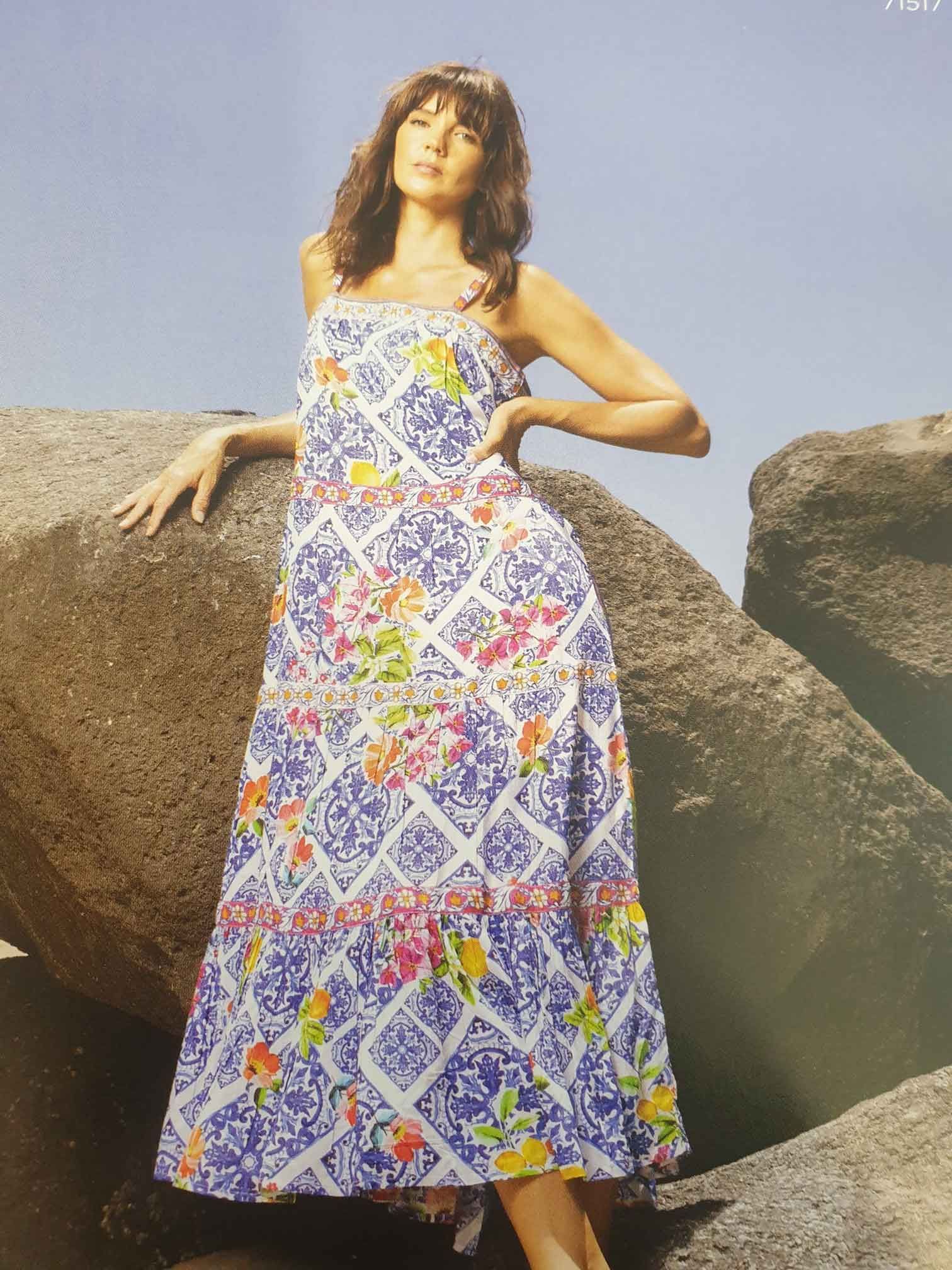 Woman wearing a blue and white floral maxi dress, posing on rocks.