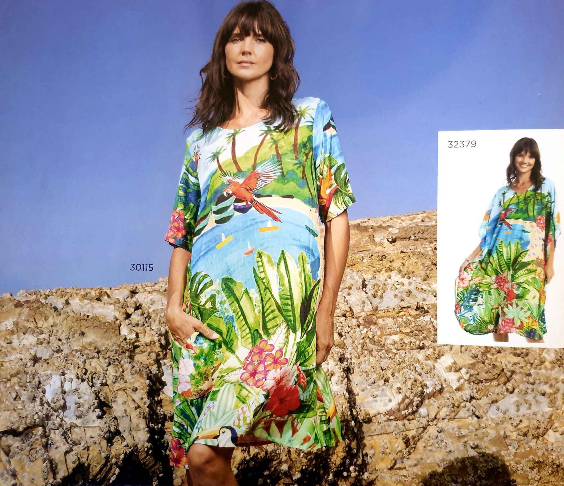 Woman in a tropical print dress, standing outdoors near rocks, looking at the camera.