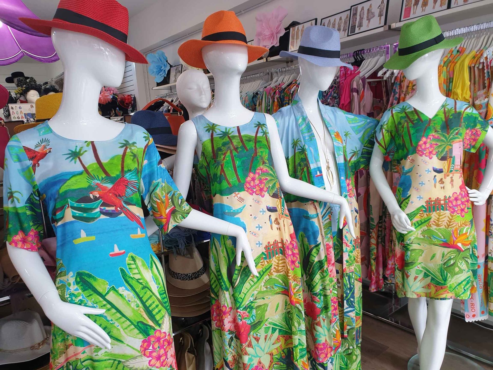 Four mannequins wearing tropical-print dresses and hats, displayed in a clothing store.