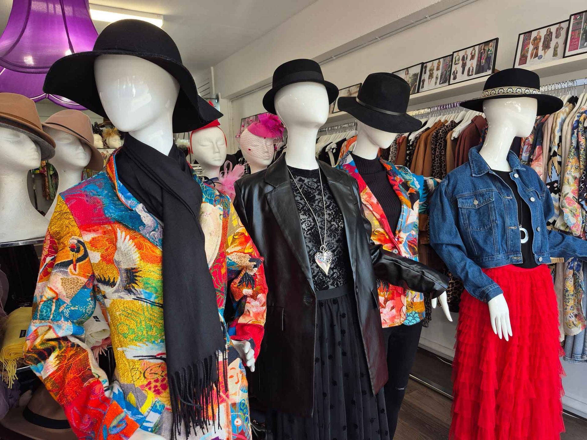Mannequins in a vintage clothing shop wearing hats, coats, and skirts. Brightly colored, diverse outfits.