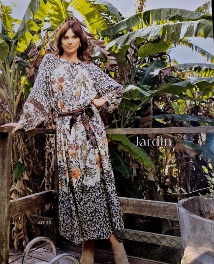 Woman in floral dress on a wooden deck; Jardin sign, lush green foliage background.