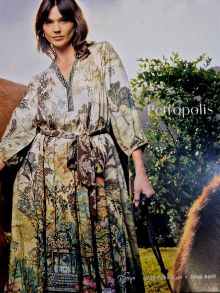 Woman in long, patterned dress holding reins, standing near a horse. Outdoors.