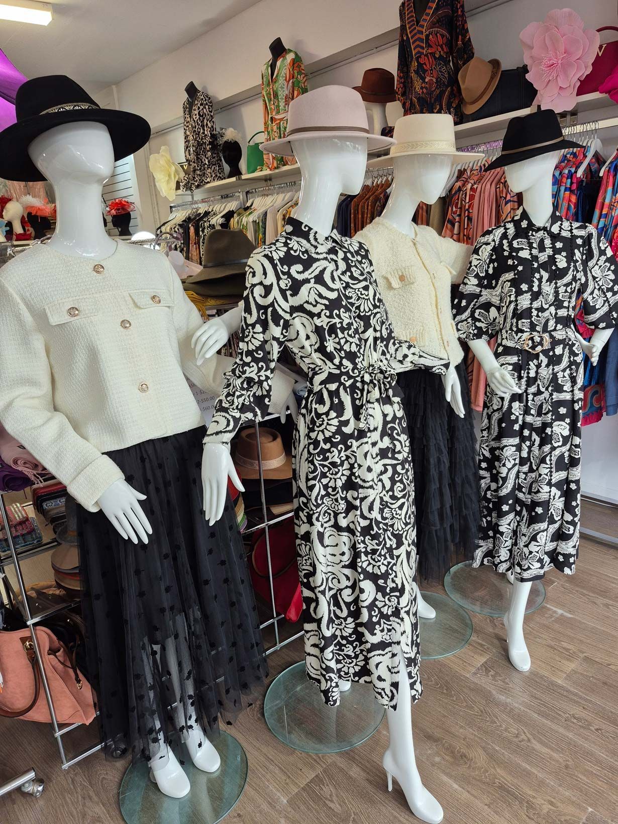 Four mannequins in a shop window wearing dresses and hats. A black and white color scheme is featured.