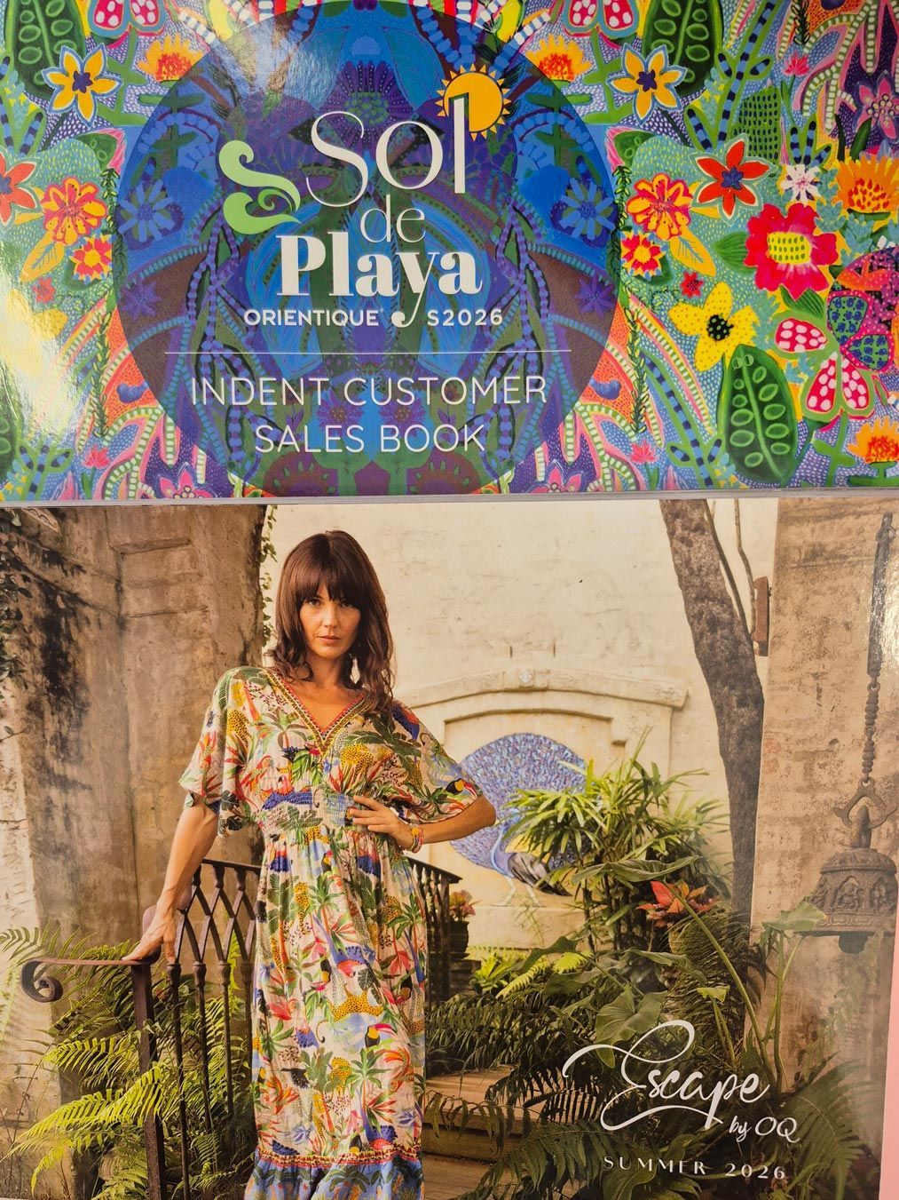 Woman in floral dress, standing next to a gate. Sales book cover for Sol de Playa boutique.