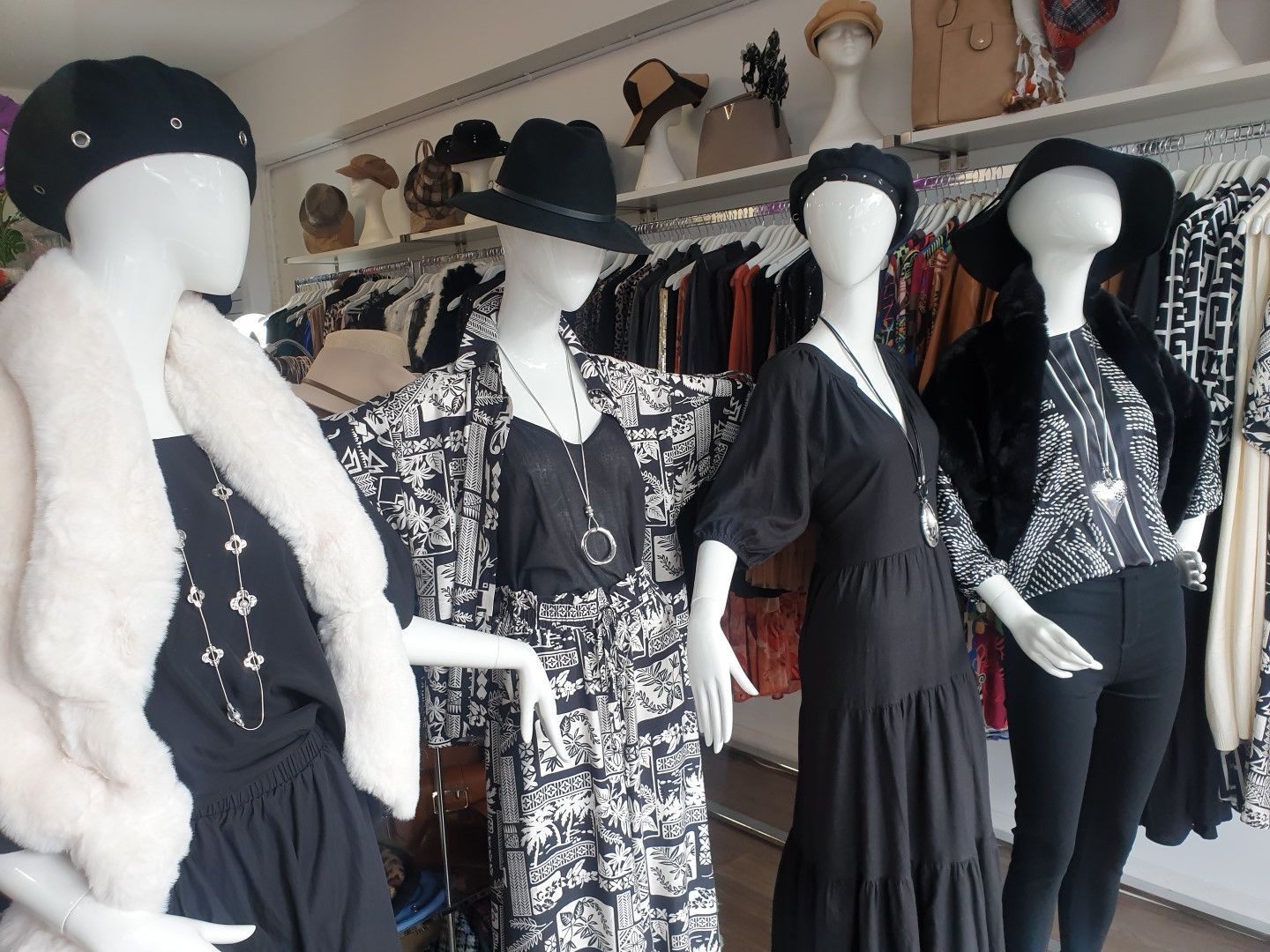 Four mannequins in a clothing store; all wearing black and white outfits, hats, and necklaces.