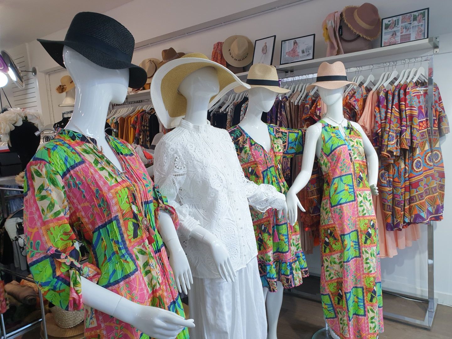 Four mannequins in a clothing store wearing colorful dresses and hats. Store racks in the background.