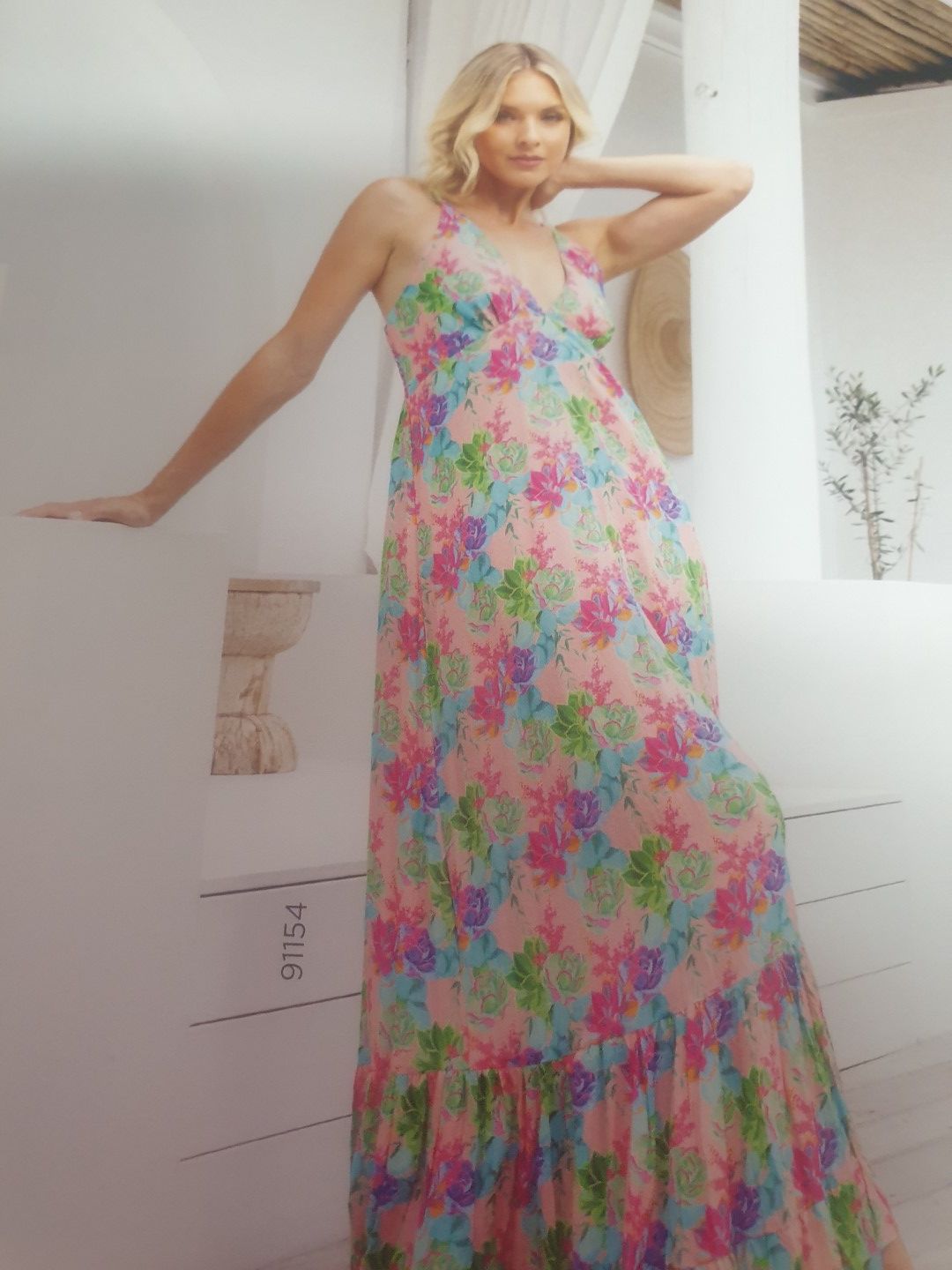 Woman in floral maxi dress, posing on a white staircase; pale pink, blue, and green colors.
