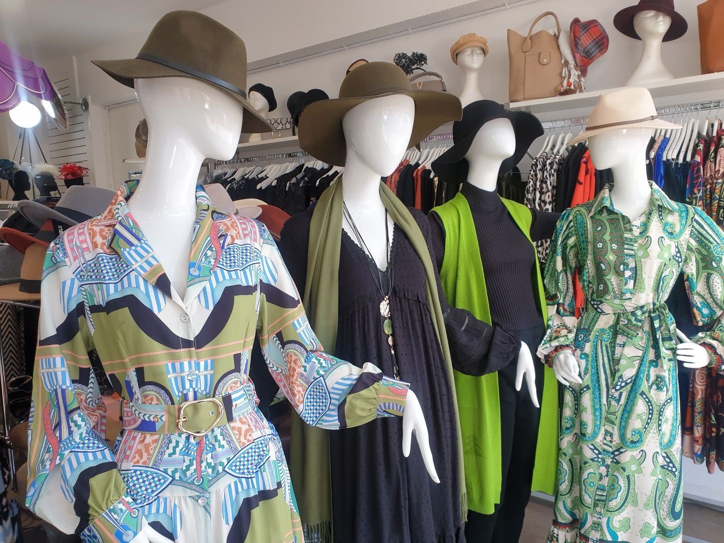 Mannequins in a boutique showcase colorful dresses and various hats.
