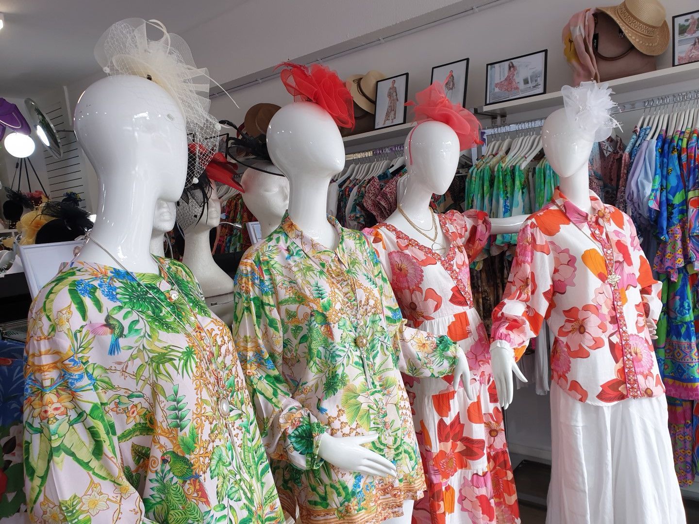 Mannequins wearing floral tops and white skirts; shop display.