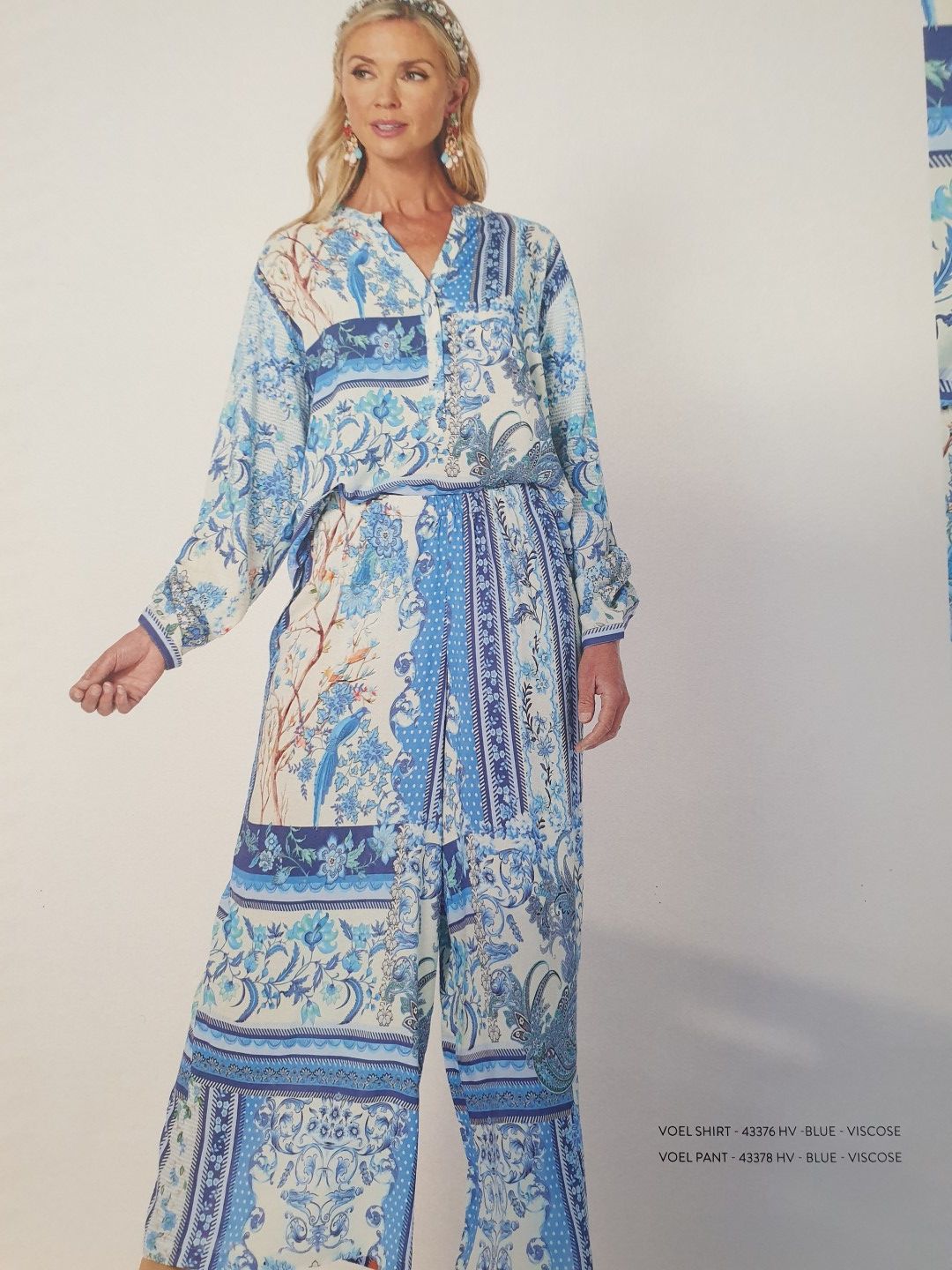 Woman in a blue and white printed jumpsuit. She has blonde hair and is smiling.