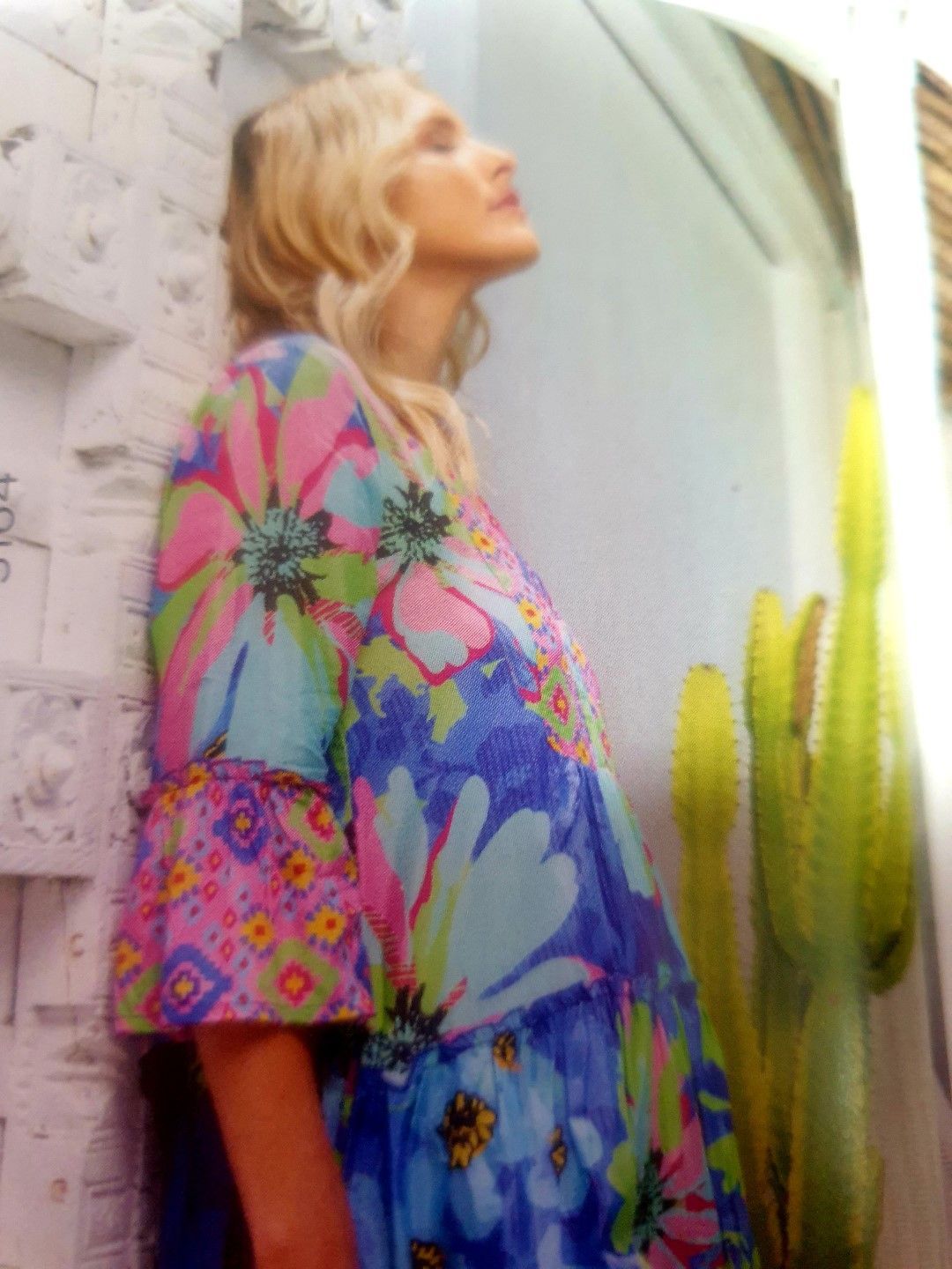 Woman in floral dress looks up near cactus.