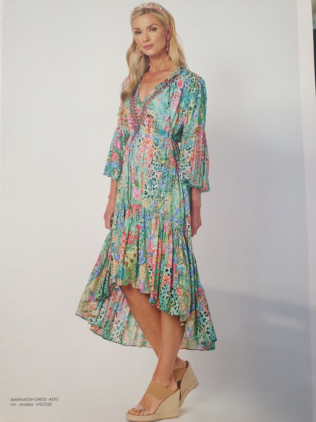 Woman in colorful floral dress, wedge heels, posing on white background.