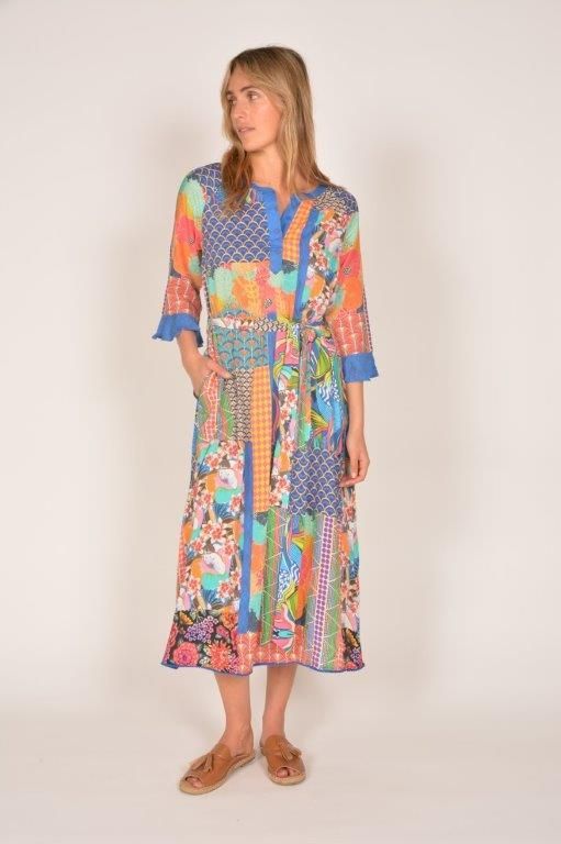 Woman wearing a colorful patchwork midi dress with a tie belt; standing, light background.