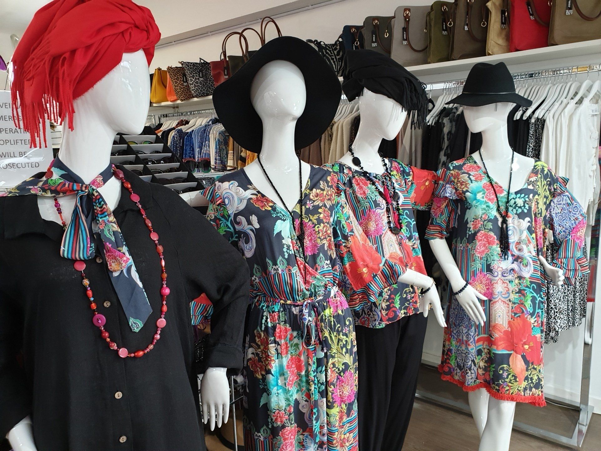 Four mannequins wearing colorful dresses and hats in a clothing store.