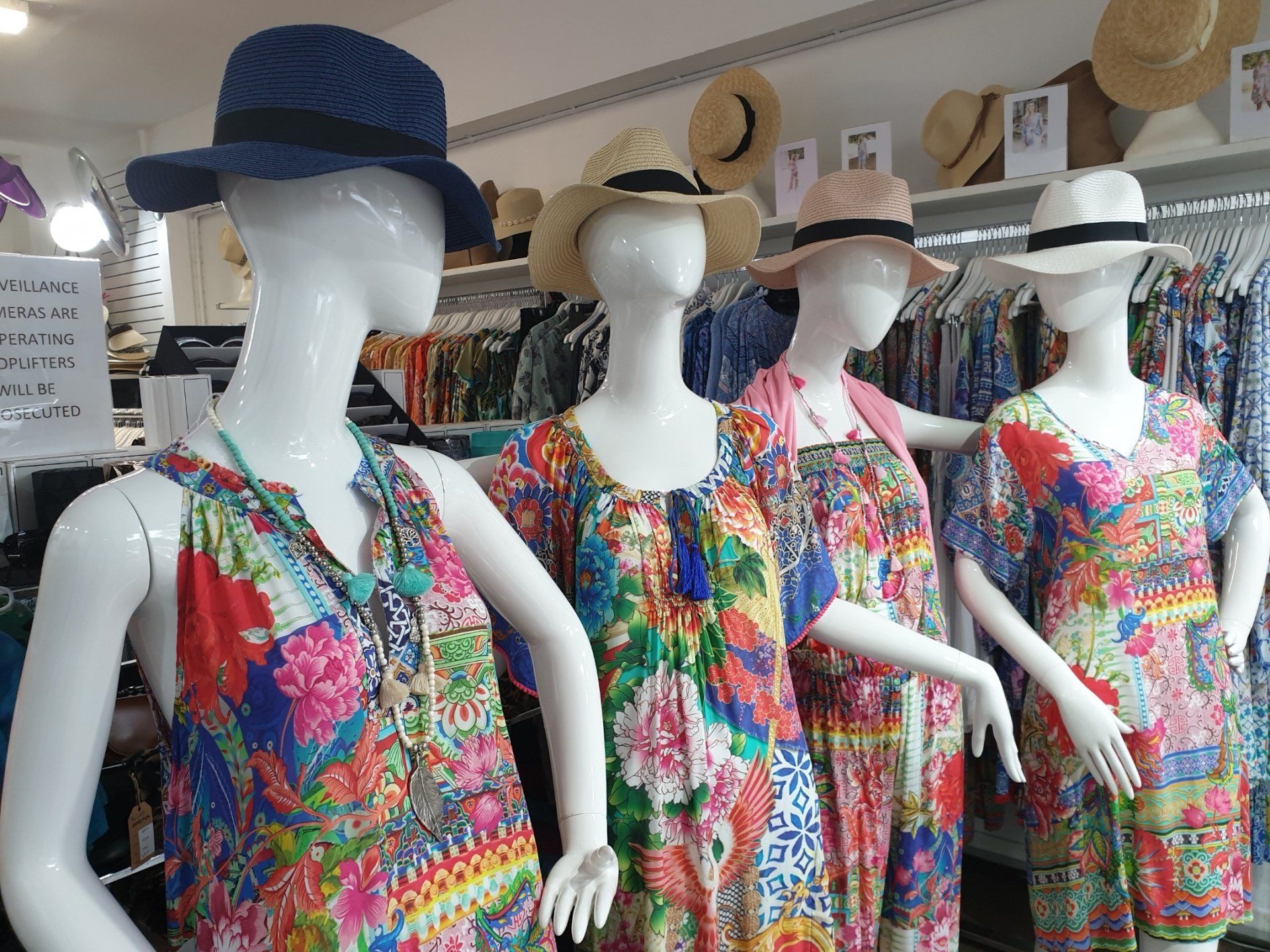Four mannequins in colorful floral dresses, wearing hats, in a clothing store.