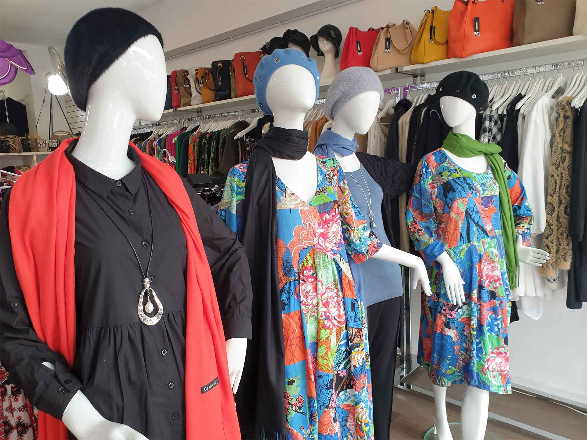 Mannequins in a clothing store display dresses, scarves, and accessories. A rack of clothing and purses are visible.