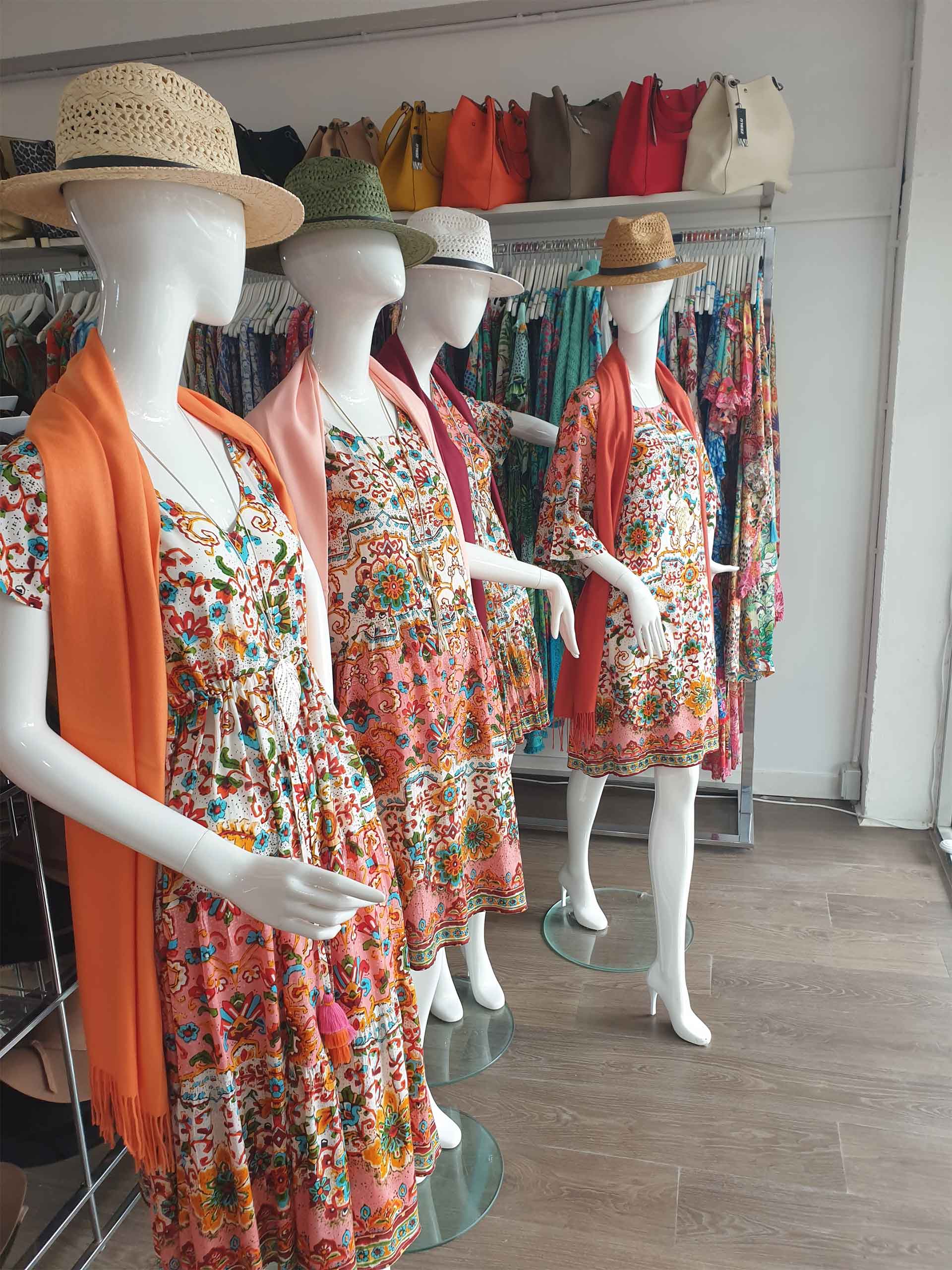 Four mannequins in floral dresses, hats, and scarves in a clothing store.