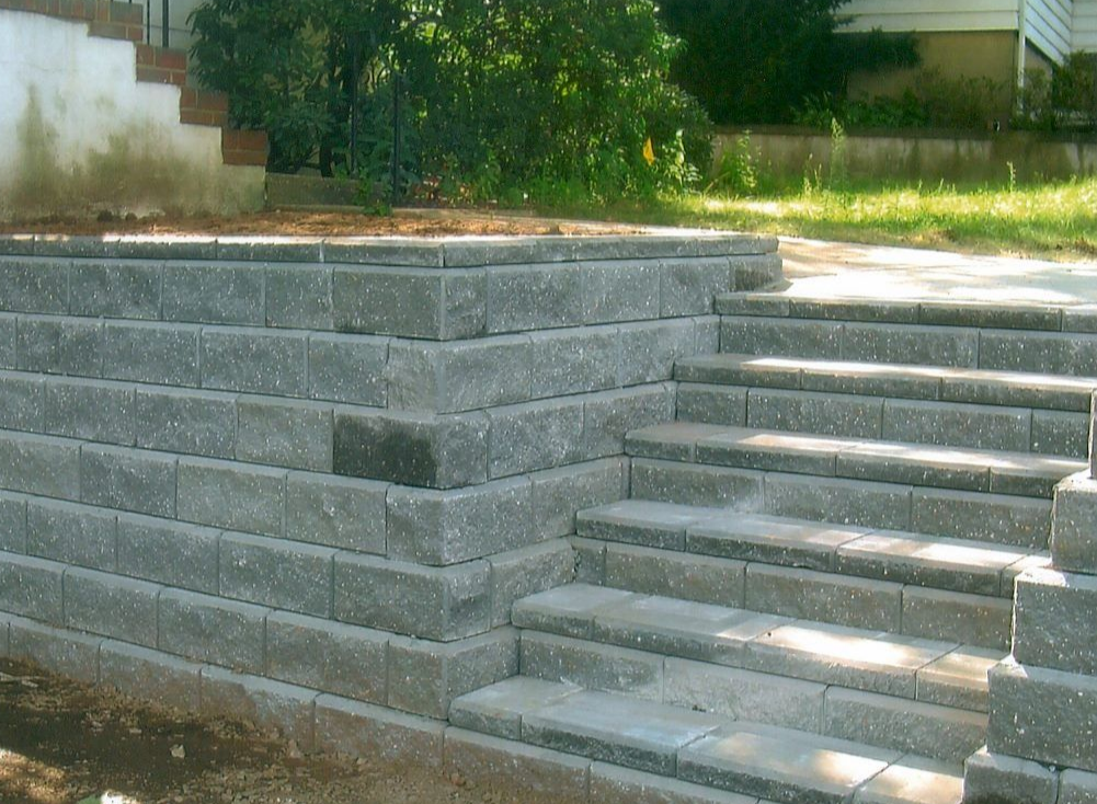 Gray block retaining wall with steps leading up to an elevated area, outdoor setting.