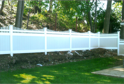 White vinyl fence in a backyard with trees and green grass.