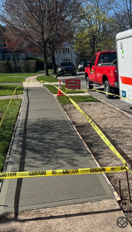 Sidewalk with newly poured concrete, under construction, bordered by yellow caution tape.