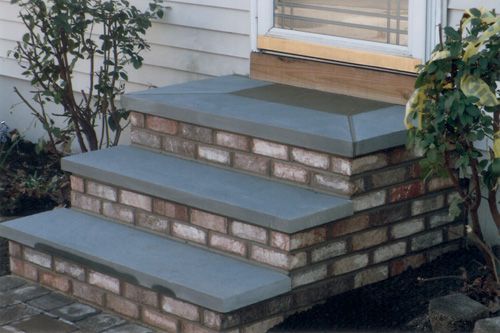Brick steps with gray stone treads leading to a door with plants on either side.