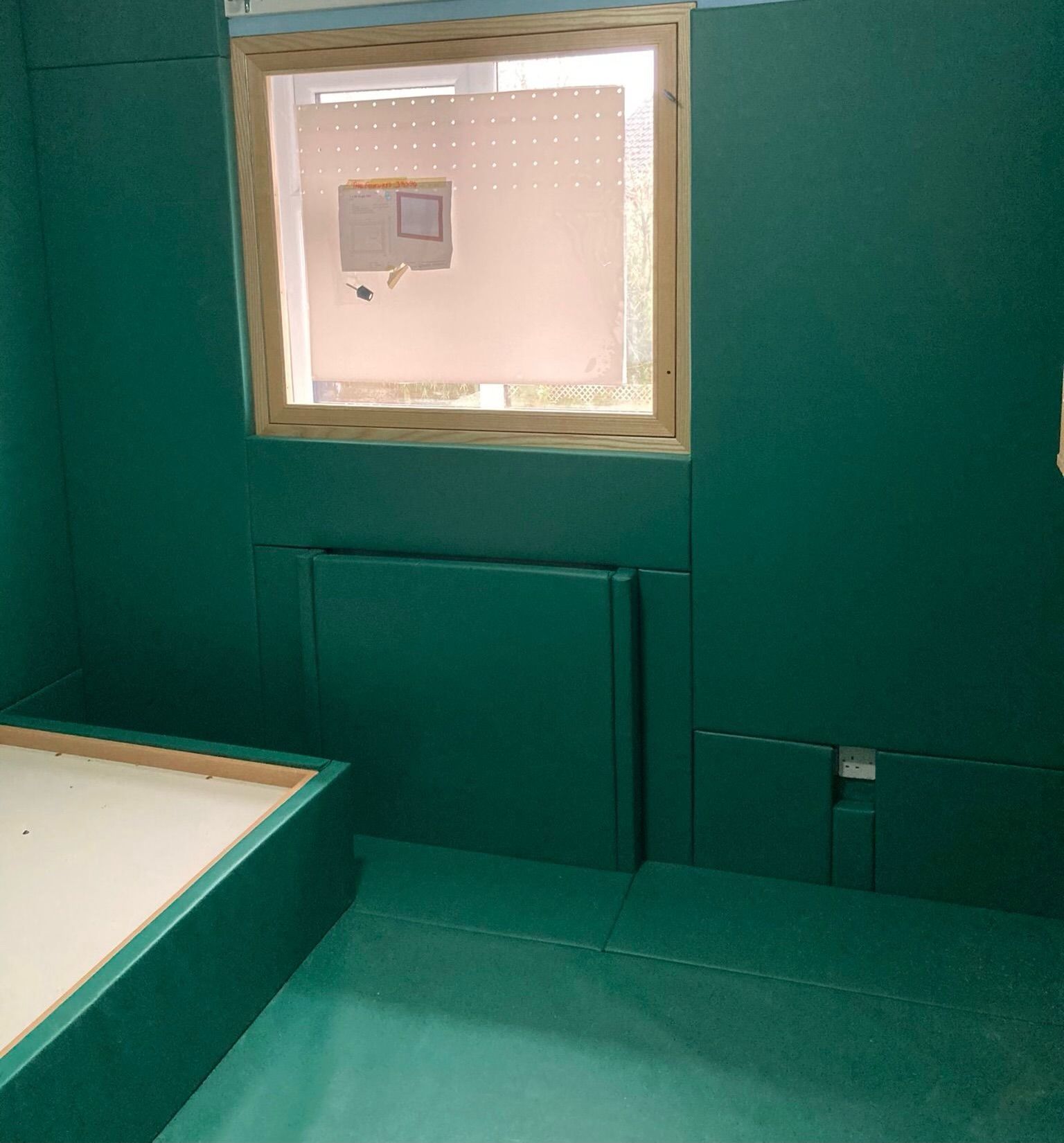 A padded room with green walls and a window