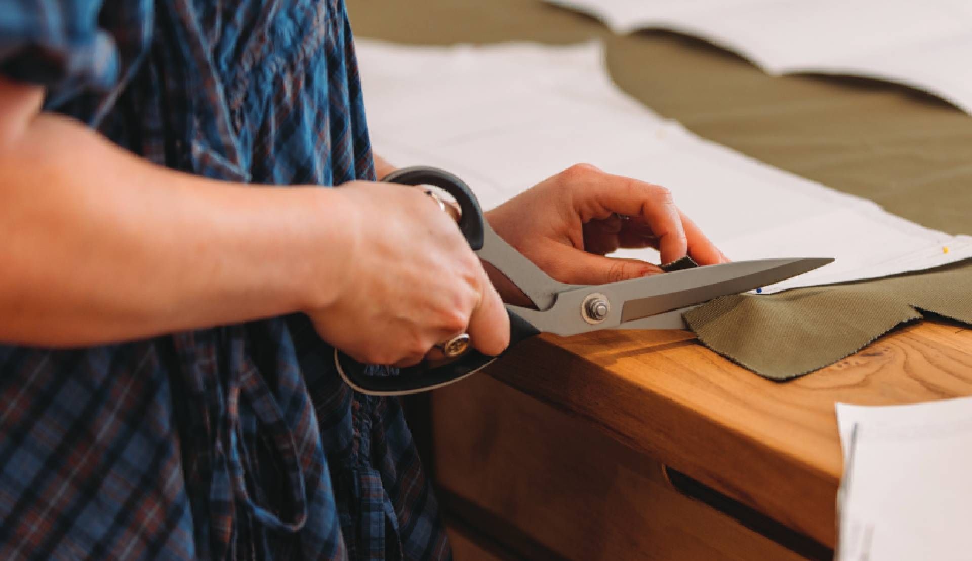 Hands cutting green fabric with scissors on a wooden table