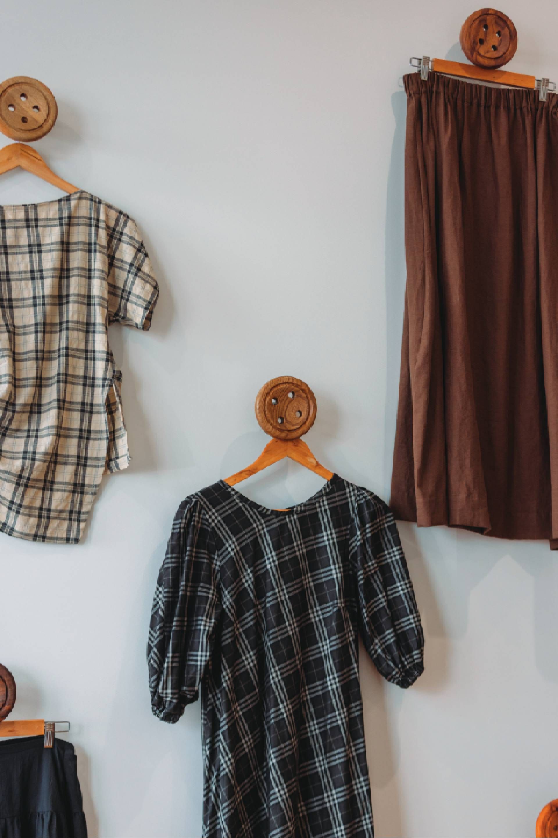 Plaid dresses and a brown skirt hanging on wooden hangers on a white wall