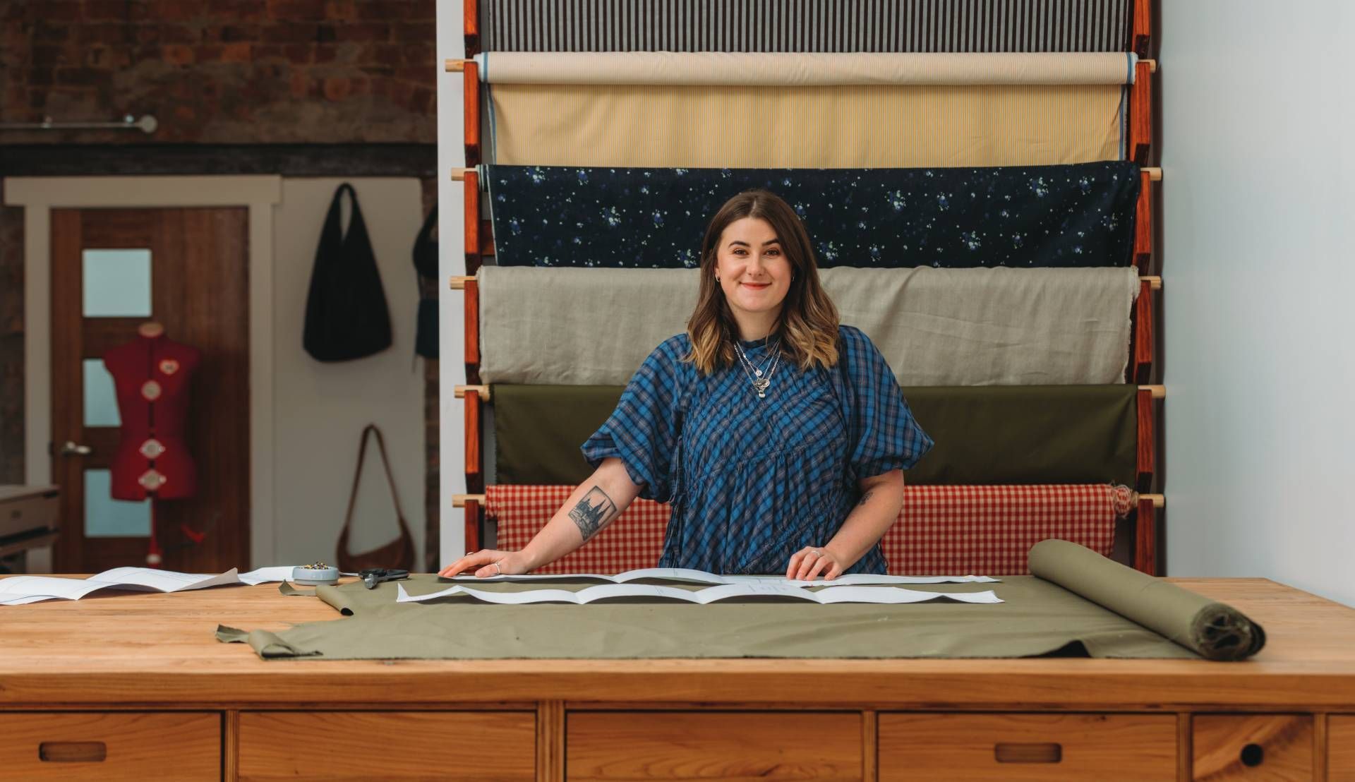 Woman standing behind a counter in a fabric shop, with rolls of fabric displayed on the wall.