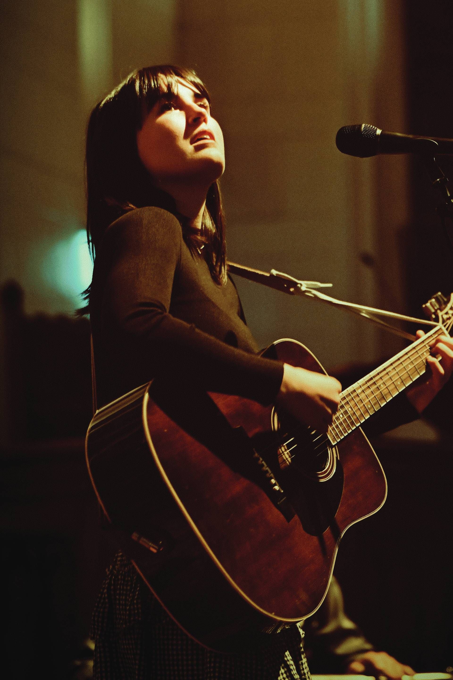 Musician singing and playing acoustic guitar onstage under warm spotlight