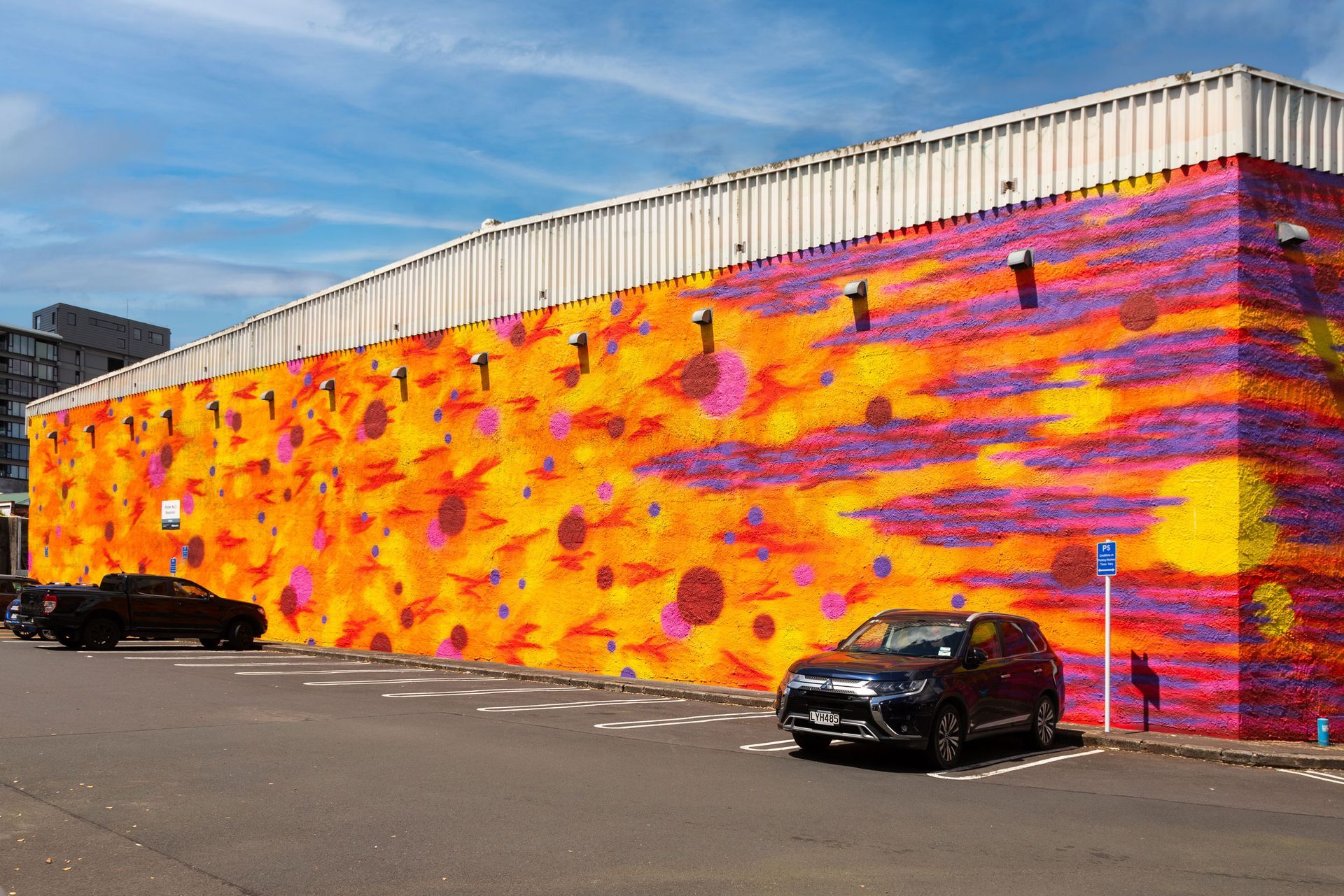 A car is parked in front of a large colorful wall.