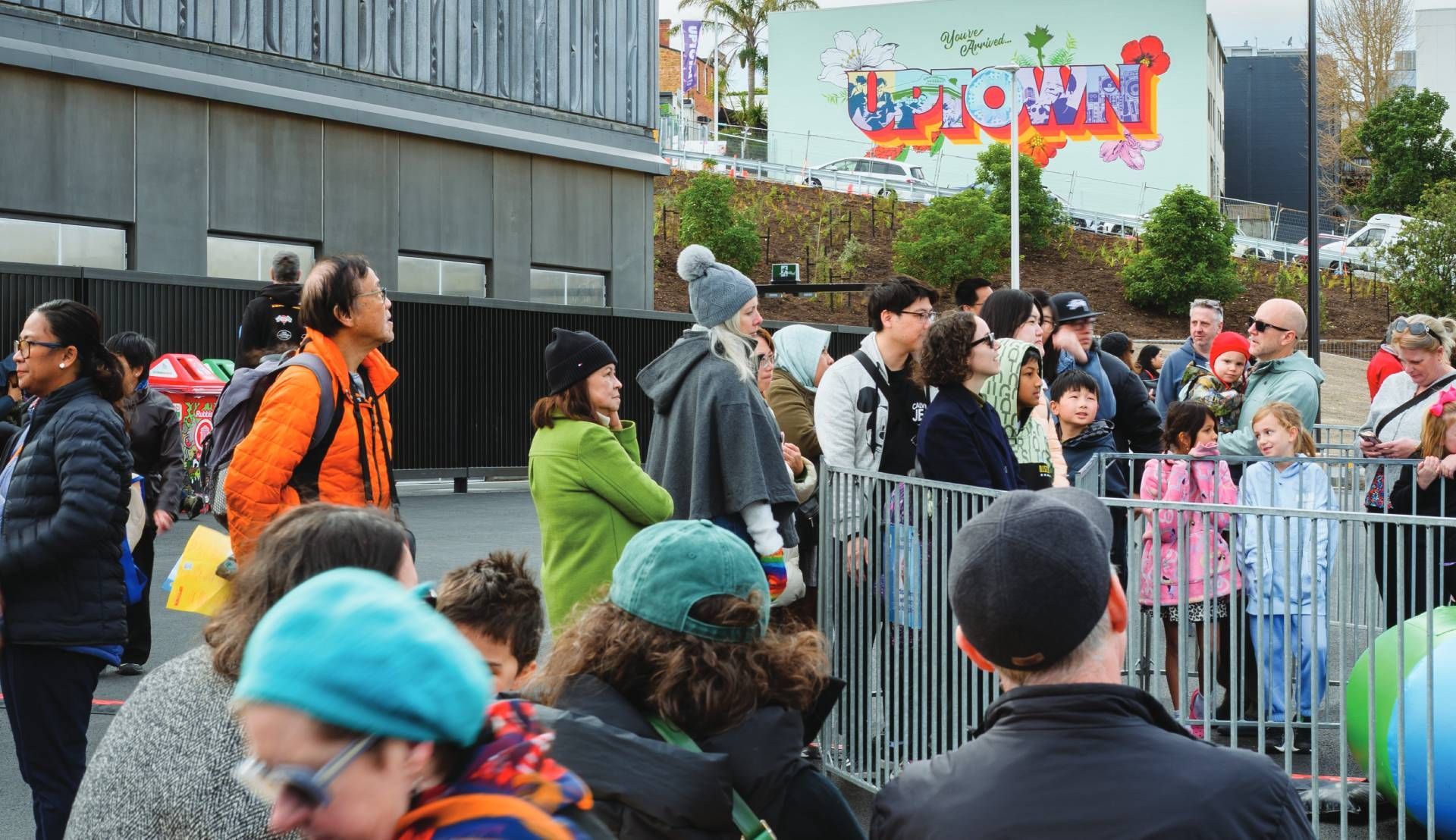 Crowd gathered behind barriers outside a building during a colorful outdoor event