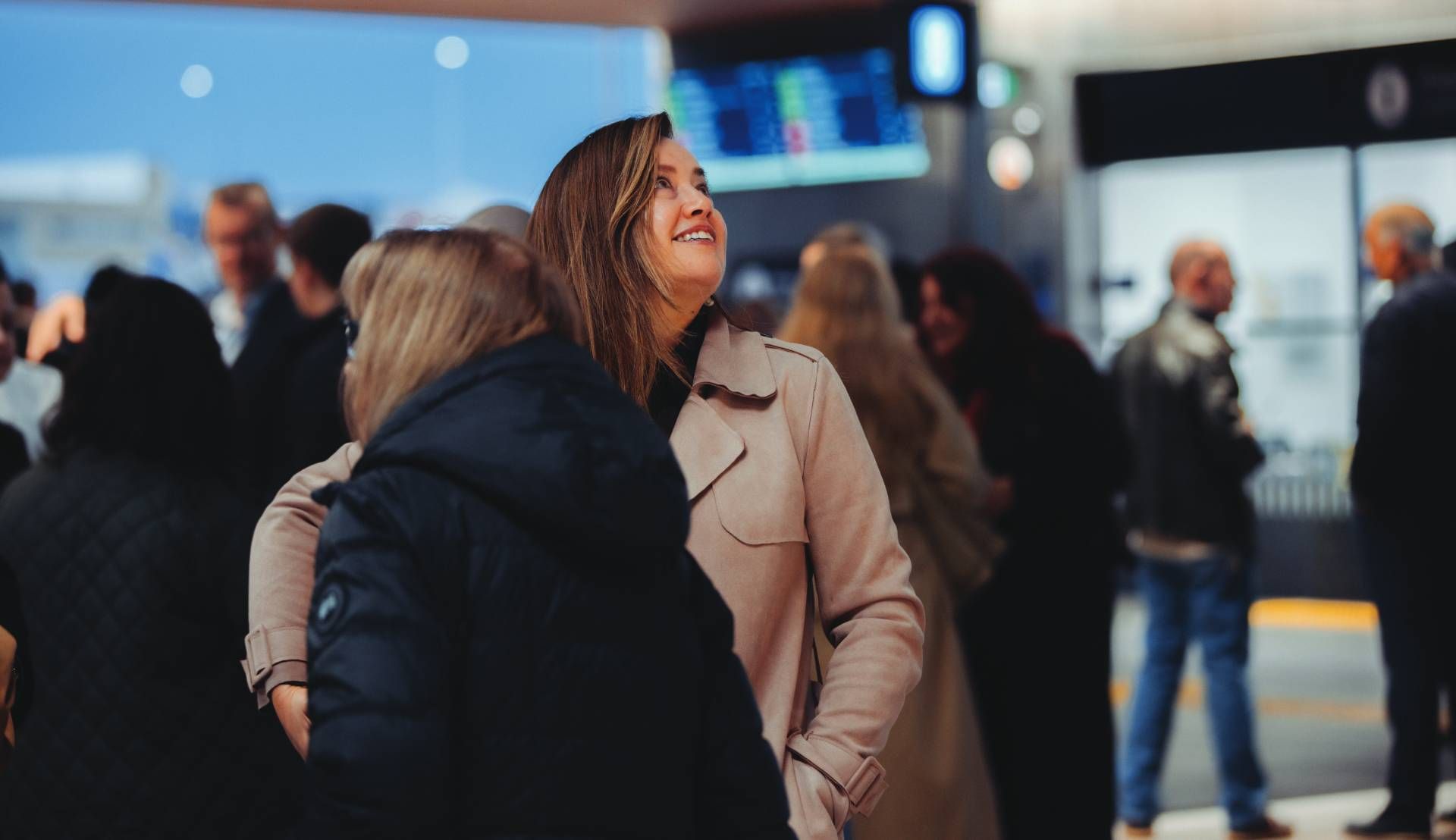 Two people embracing in a busy indoor public space, with one smiling and blurred crowds in the background.