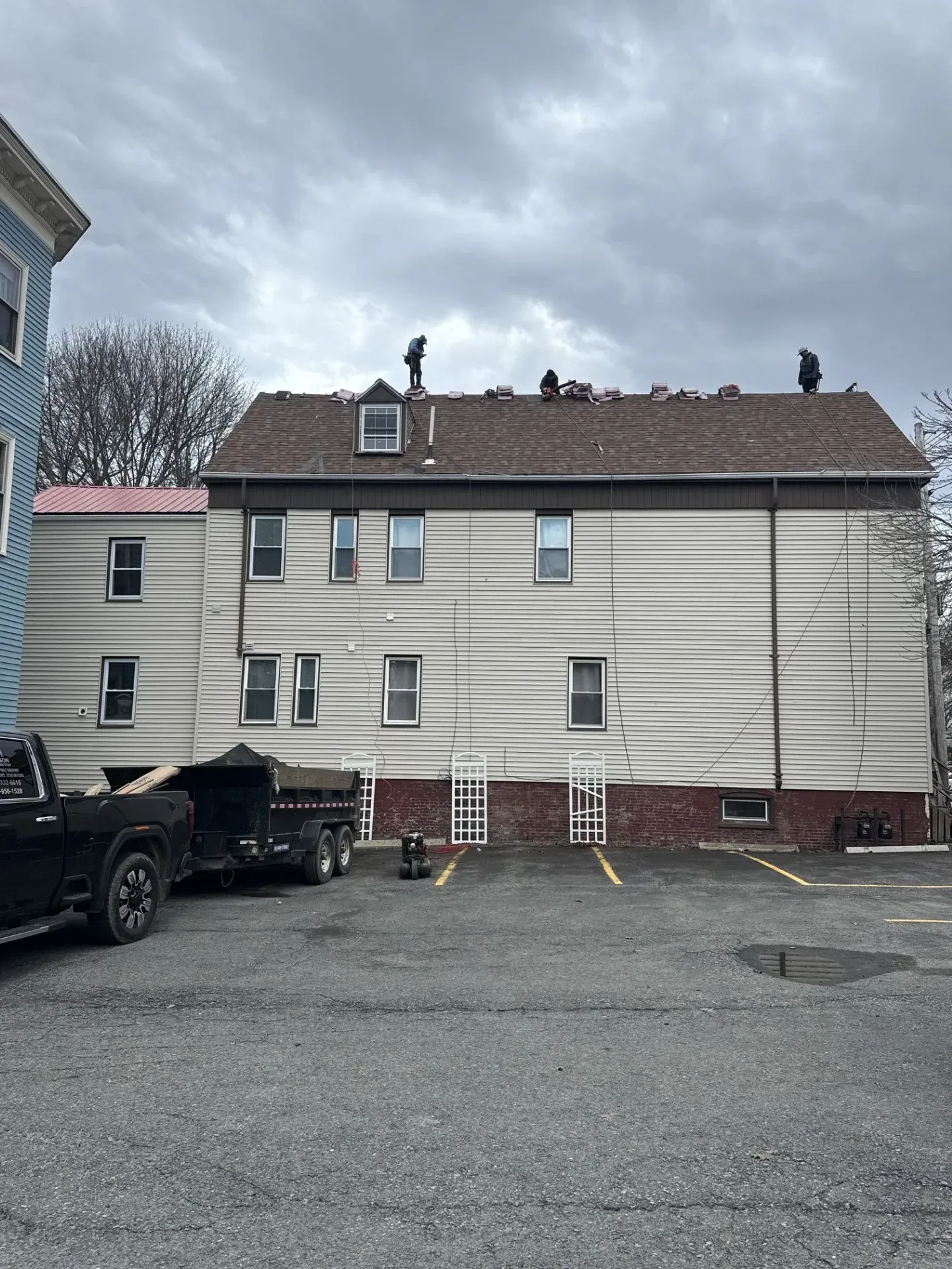 Apartment building exterior with beige siding, brick foundation, parked truck, and cloudy sky