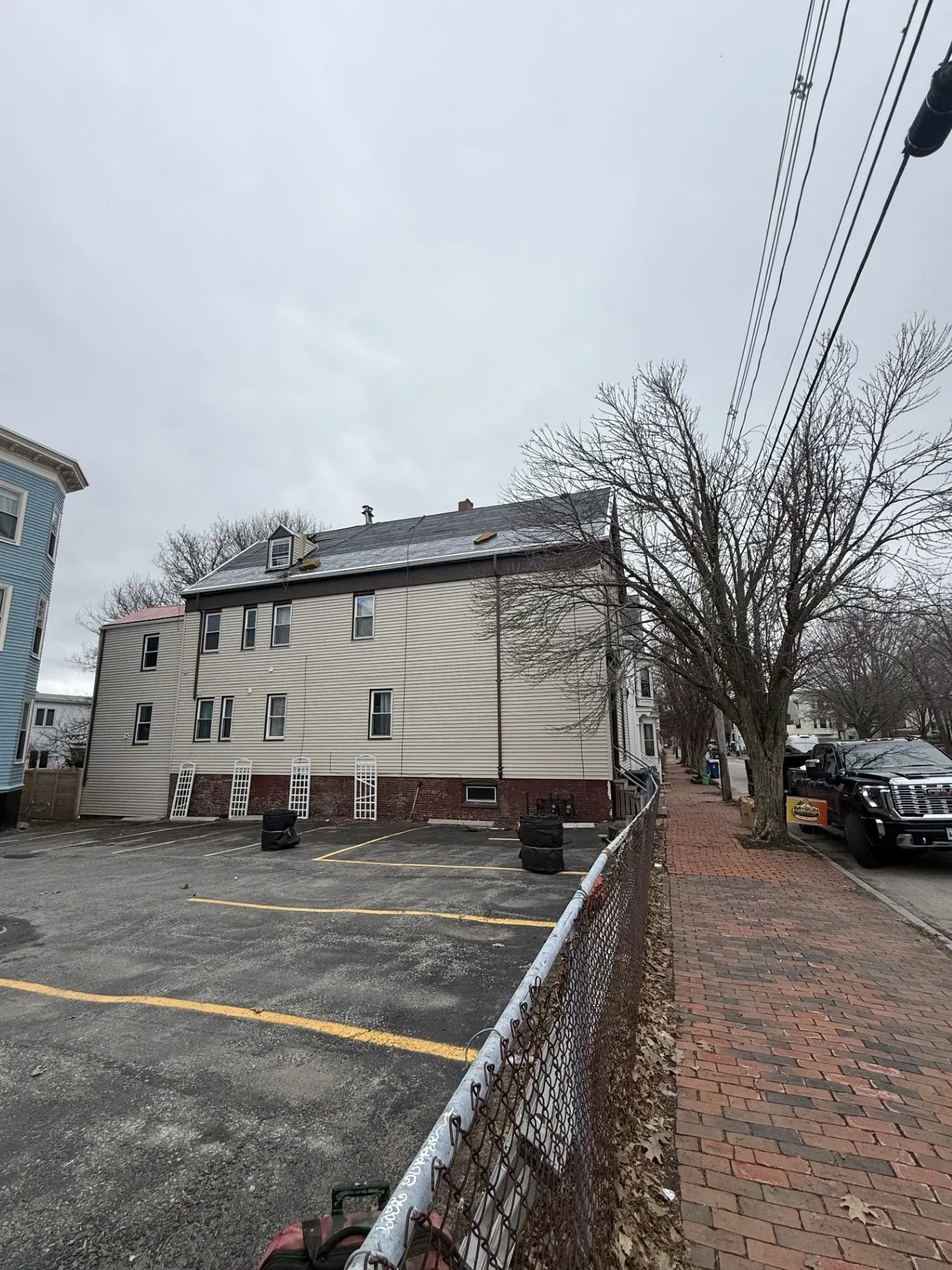 Brick sidewalk beside a beige apartment building and parking lot on a cloudy day
