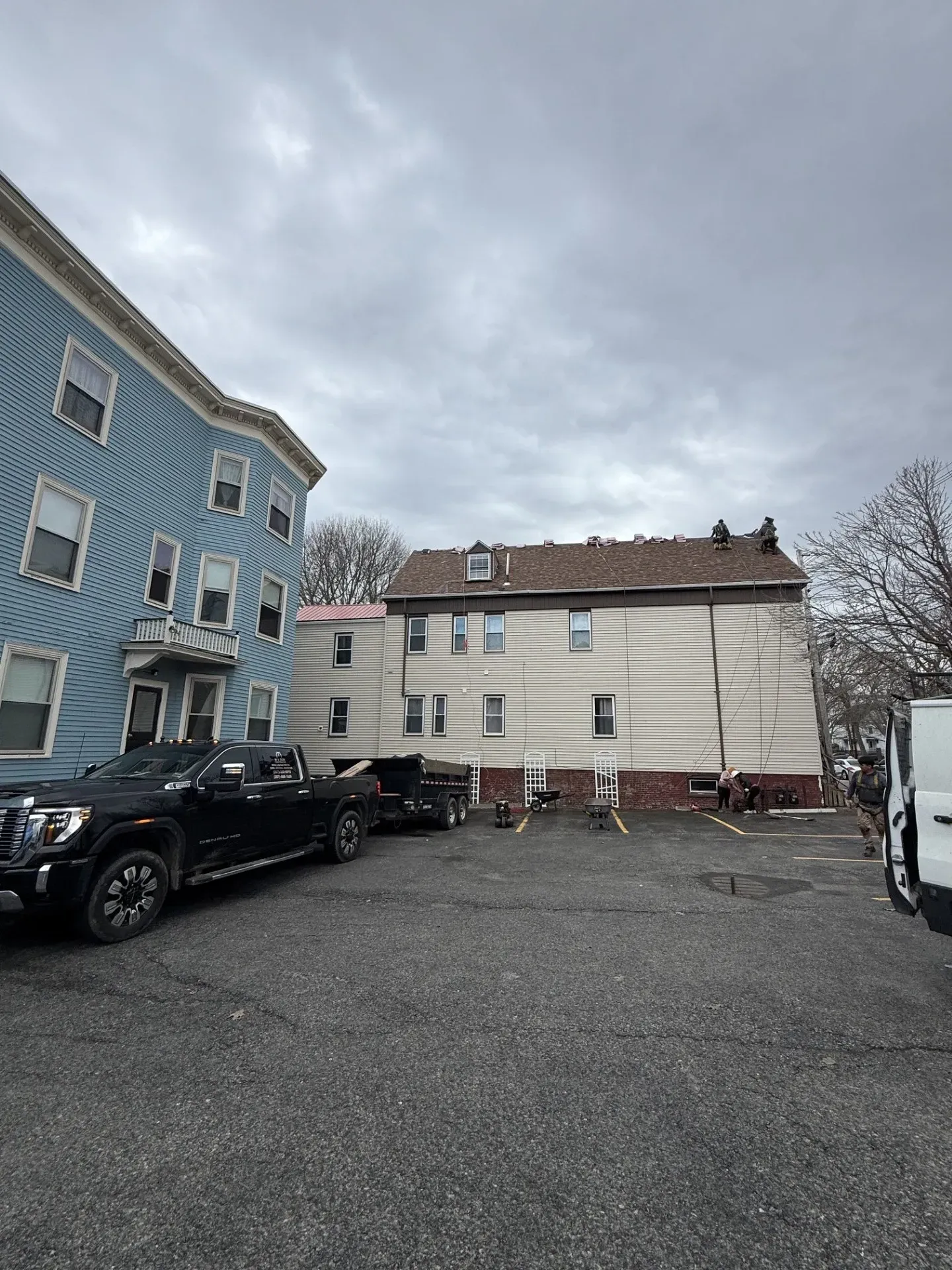 Apartment buildings and parked cars in a gravel lot under a cloudy sky