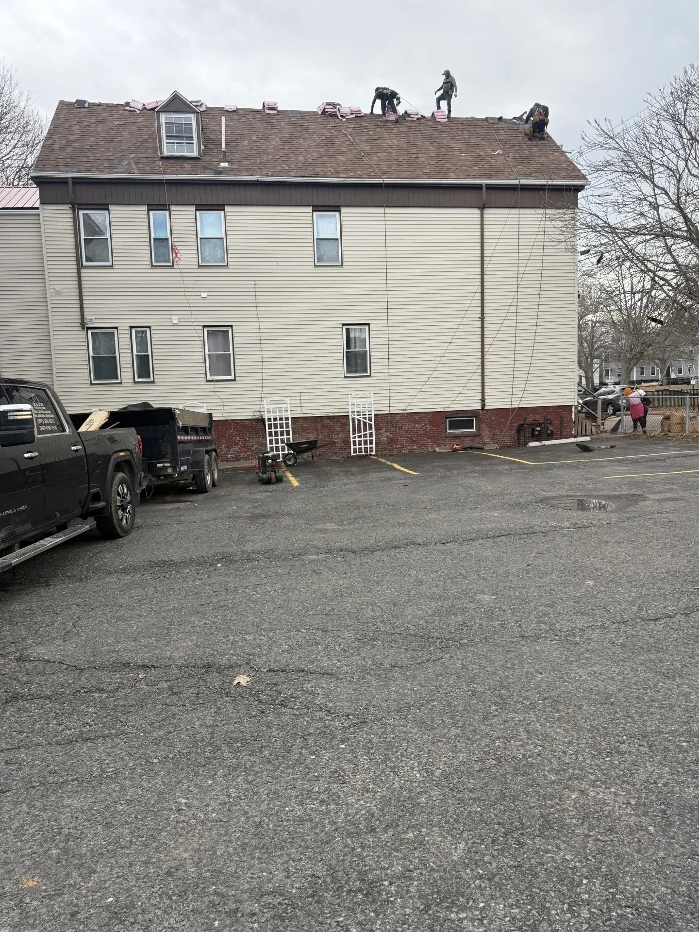 Damaged beige apartment building with workers on the roof and debris on the ground after storm damage