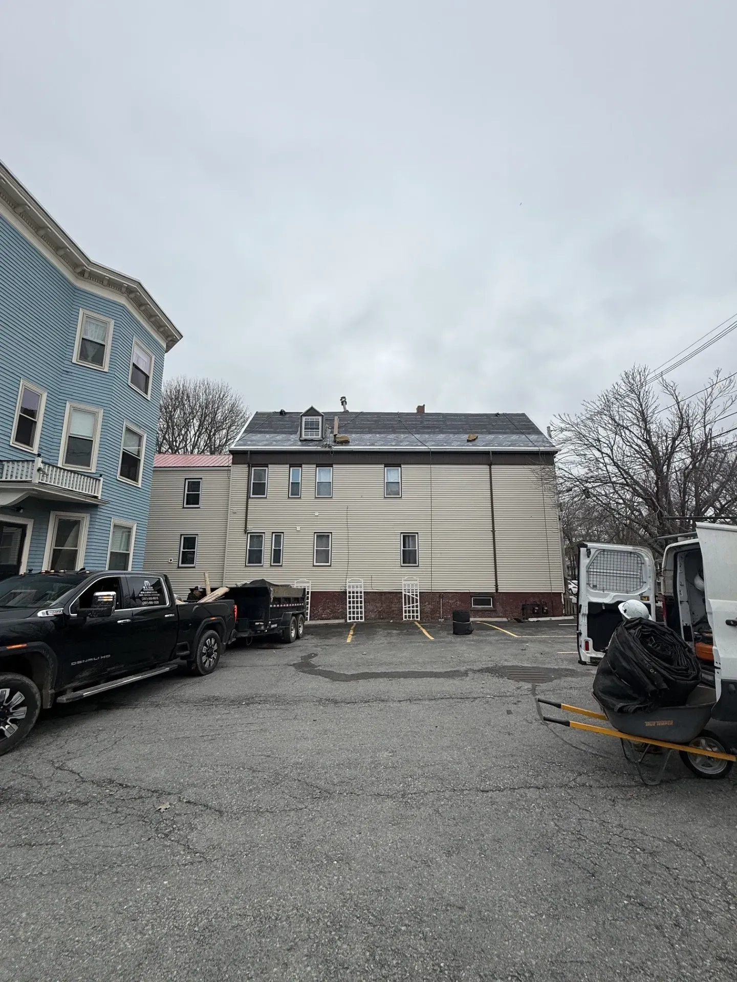 Parking lot with black trucks beside a blue building and a beige apartment building under a cloudy sky