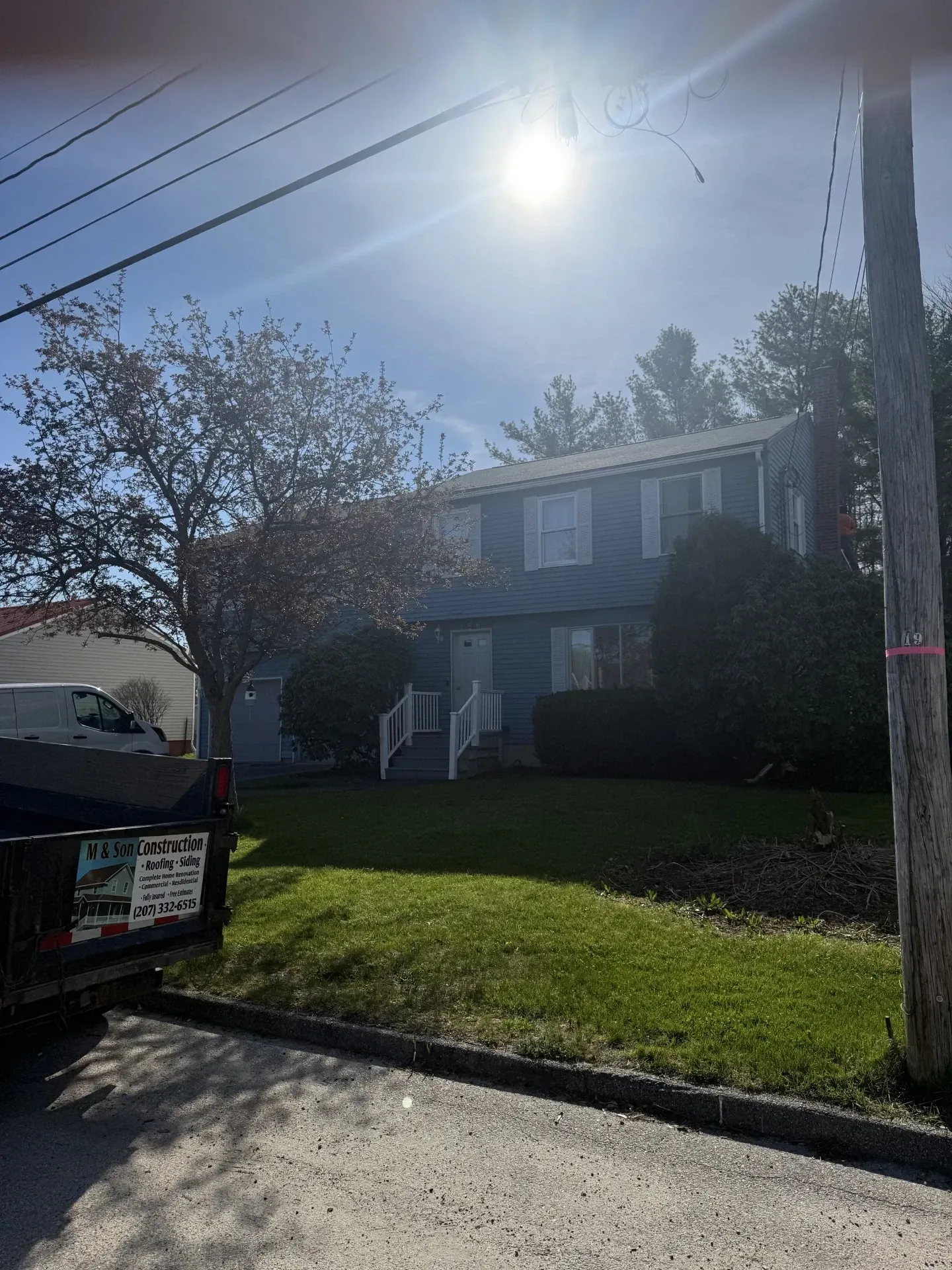 Suburban house with front lawn, parked truck, and bright sun overhead on a clear day